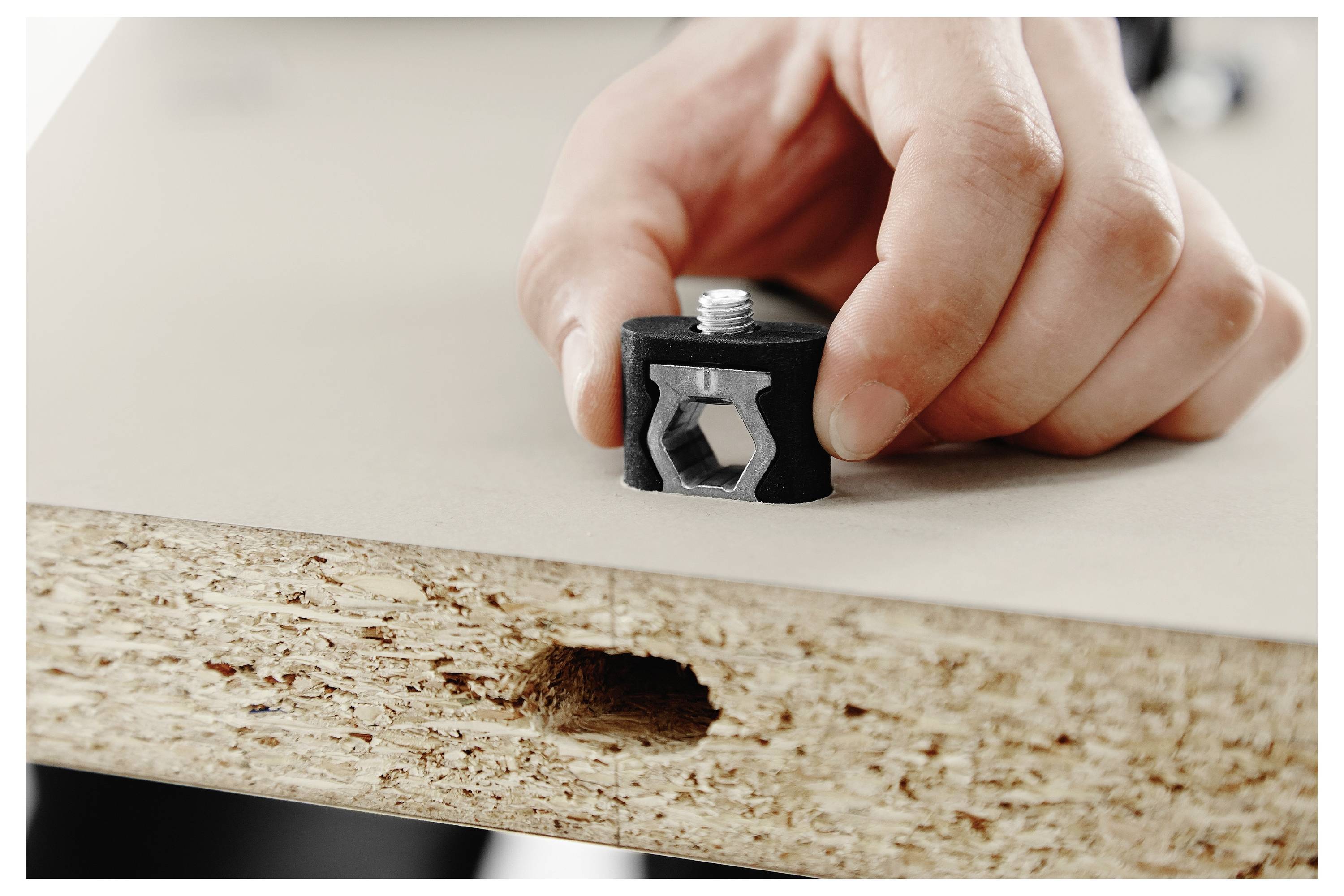Eine Hand, die einen Bolzen in einen Möbelmontageverbinder an einer Spanplattenkante einsichert, zeigt den Montageprozess von Möbeln zum Selbstaufbau.