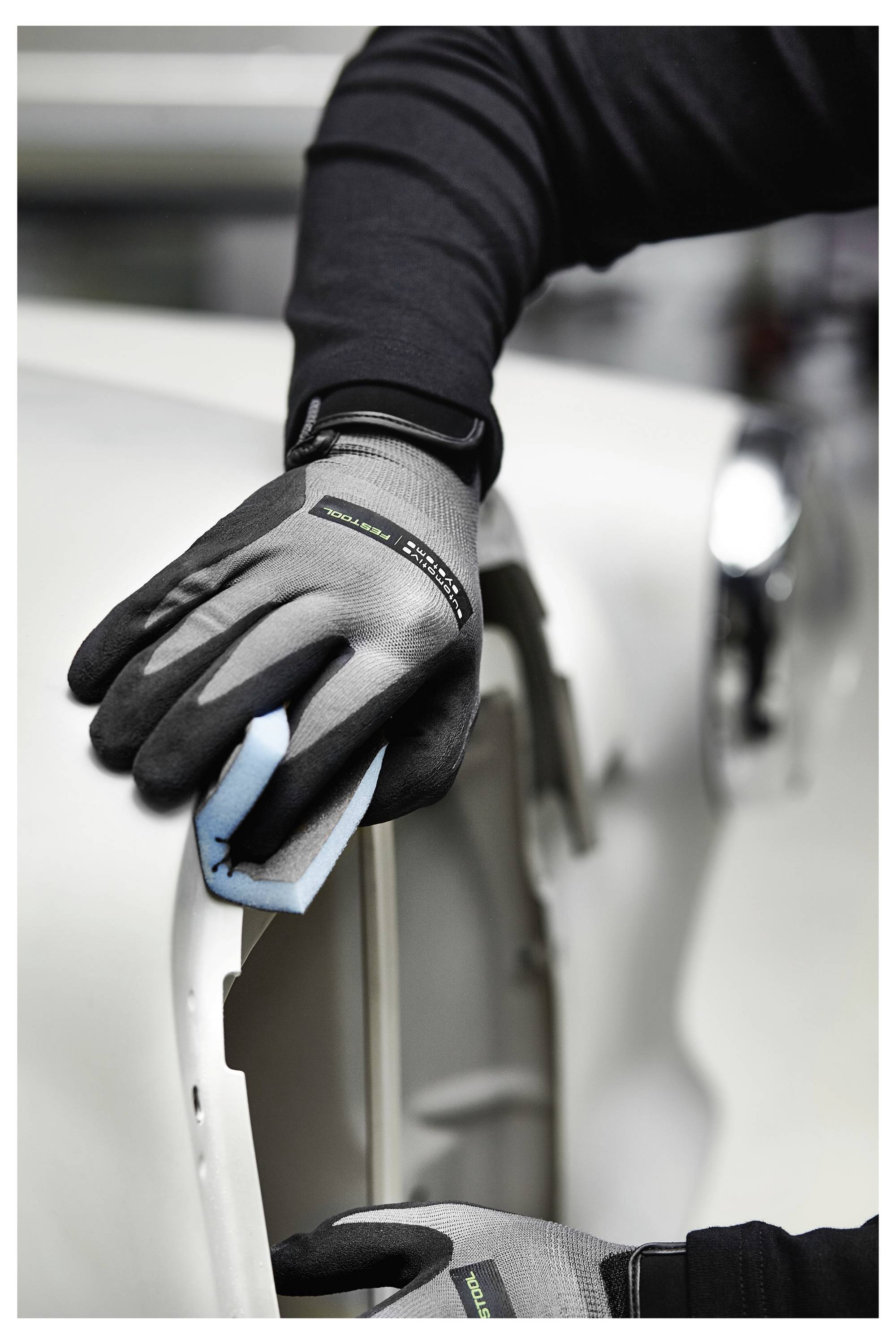 Eine Person mit Handschuhen reinigt die Außenseite eines Autos mit einem blauen Schwamm und konzentriert sich auf eine hellfarbige Fahrzeugoberfläche, wobei die Pflegedetails hervorgehoben werden.