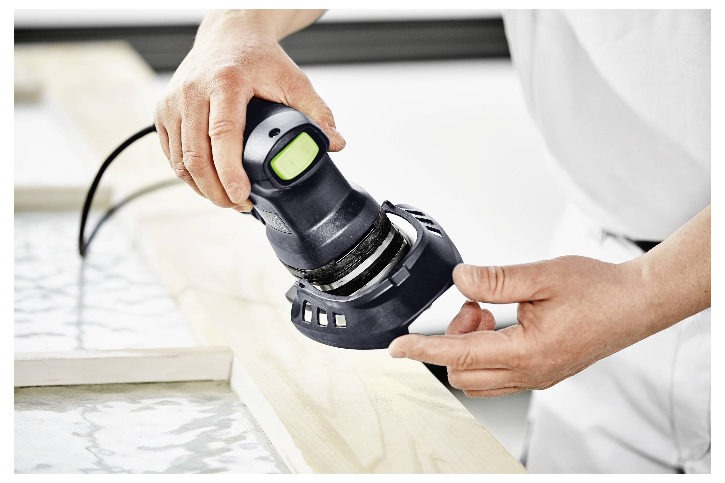 Eine Person verwendet einen tragbaren elektrischen Schleiffer, um die Oberfläche eines Holzbretts zu glätten, wobei der Fokus auf präziser Schleiftechnik liegt.