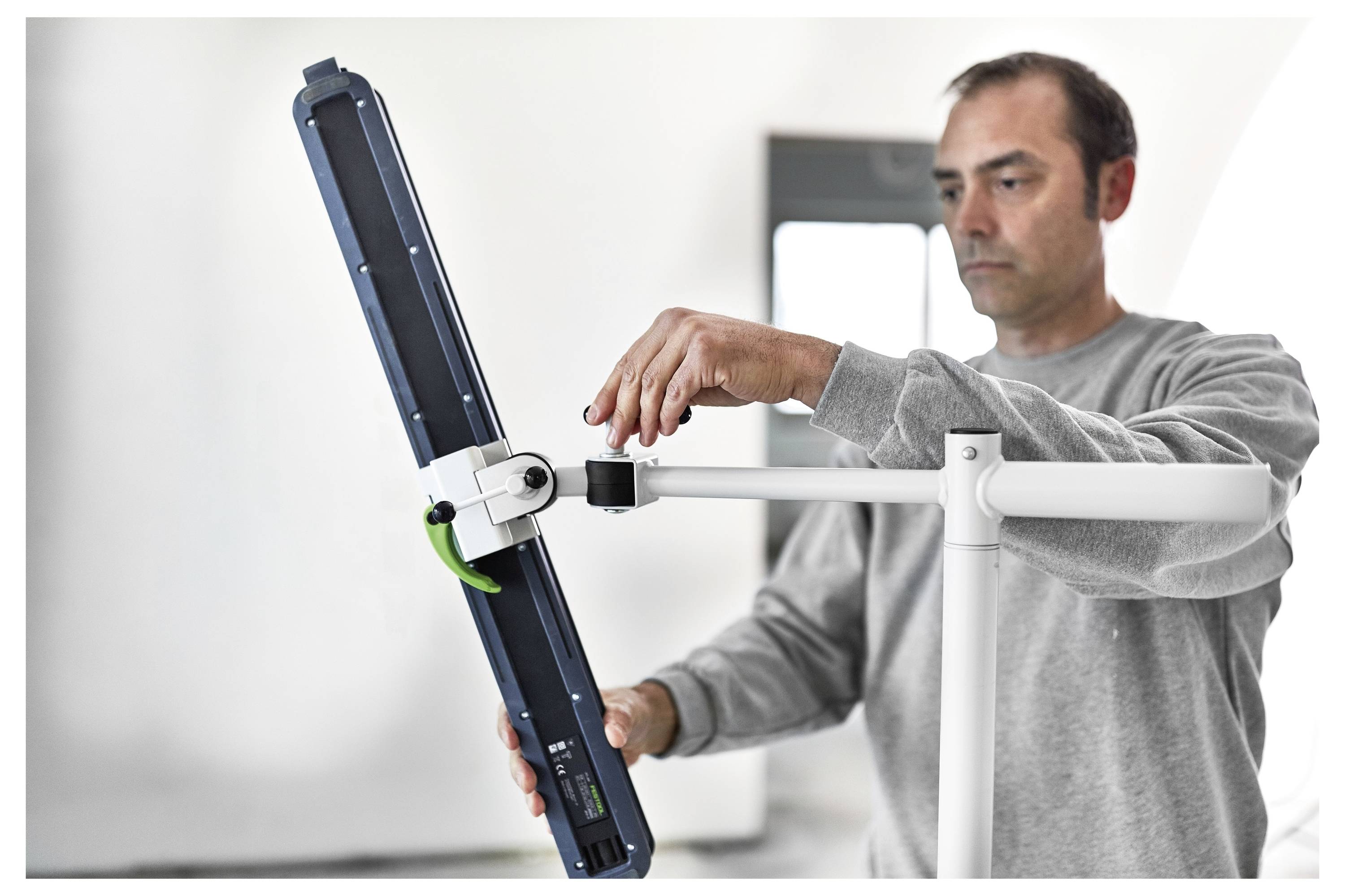 Eine Person stellt ein blaues und weißes elektronisches Gerät ein, das auf einem Ständer montiert ist, möglicherweise um es einzurichten oder zu kalibrieren, in einem hellen Raum.