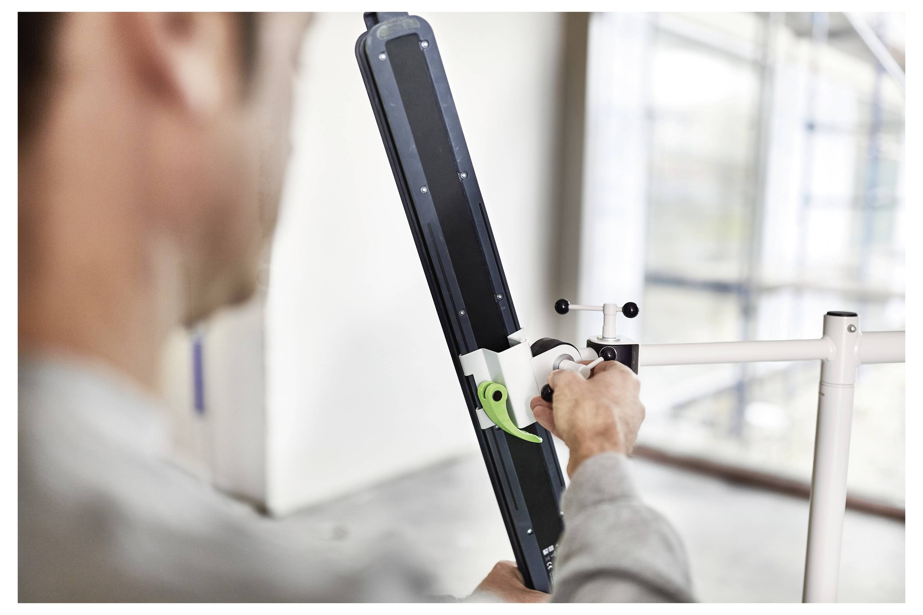 Eine Person stellt einen Fahrradreparaturständer ein und zieht eine Komponente mit einem Werkzeug fest. Die Umgebung sieht wie eine Innenwerkstatt aus.