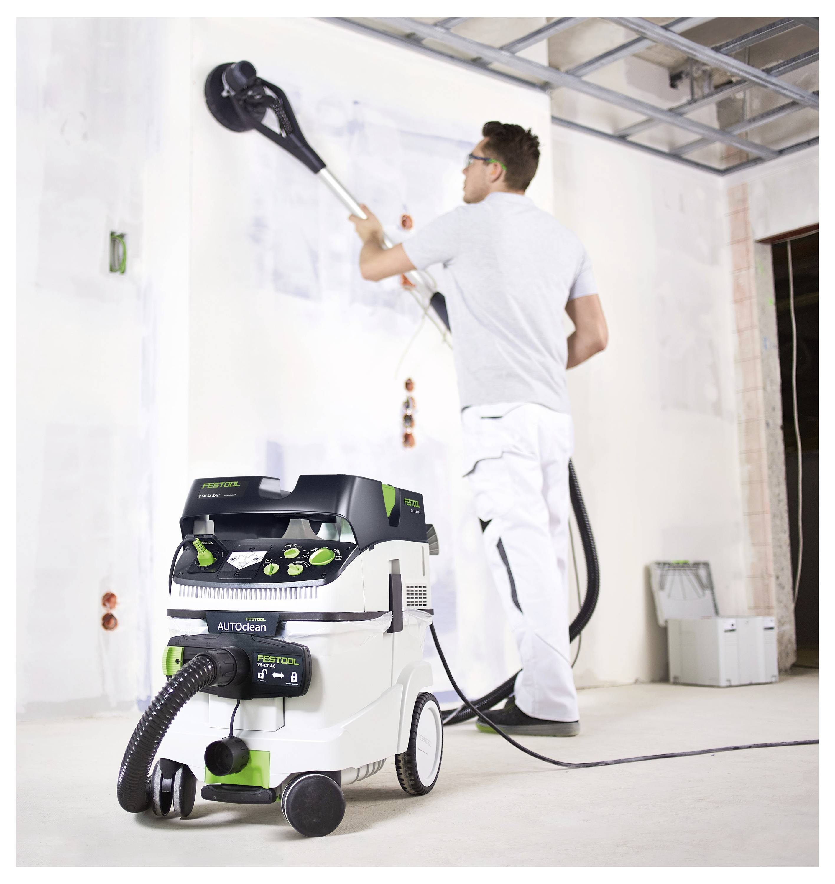 Eine Person stellt eine Spannvorrichtung an einem Werkstatt-Arbeitstisch ein und sichert damit ein Holzstück in einer hell beleuchteten Werkstatt.