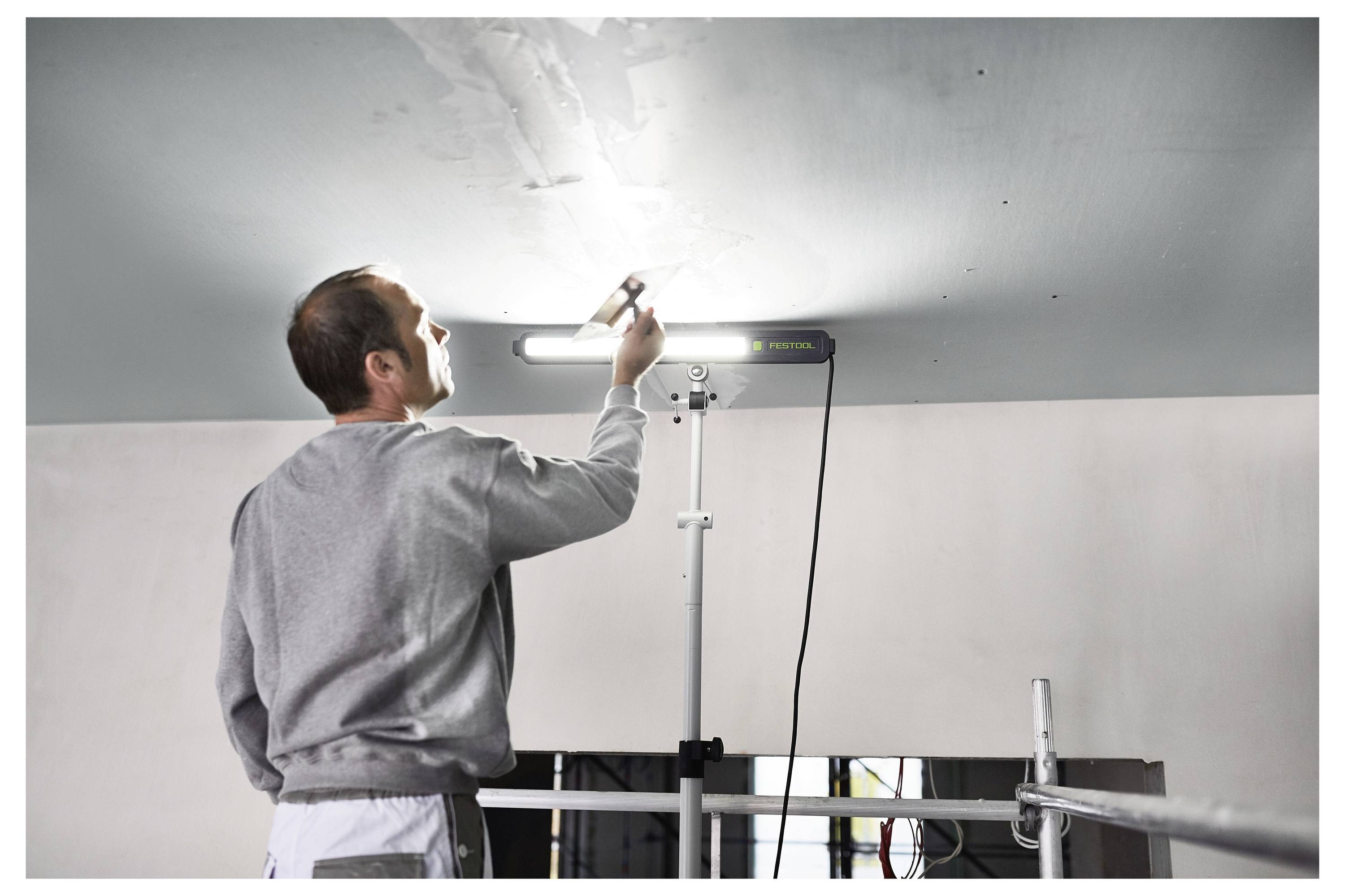 Eine Person in einem grauen Pullover inspiziert die Decke mit Hilfe einer angebrachten Leuchte in einem Renovierungszimmer.