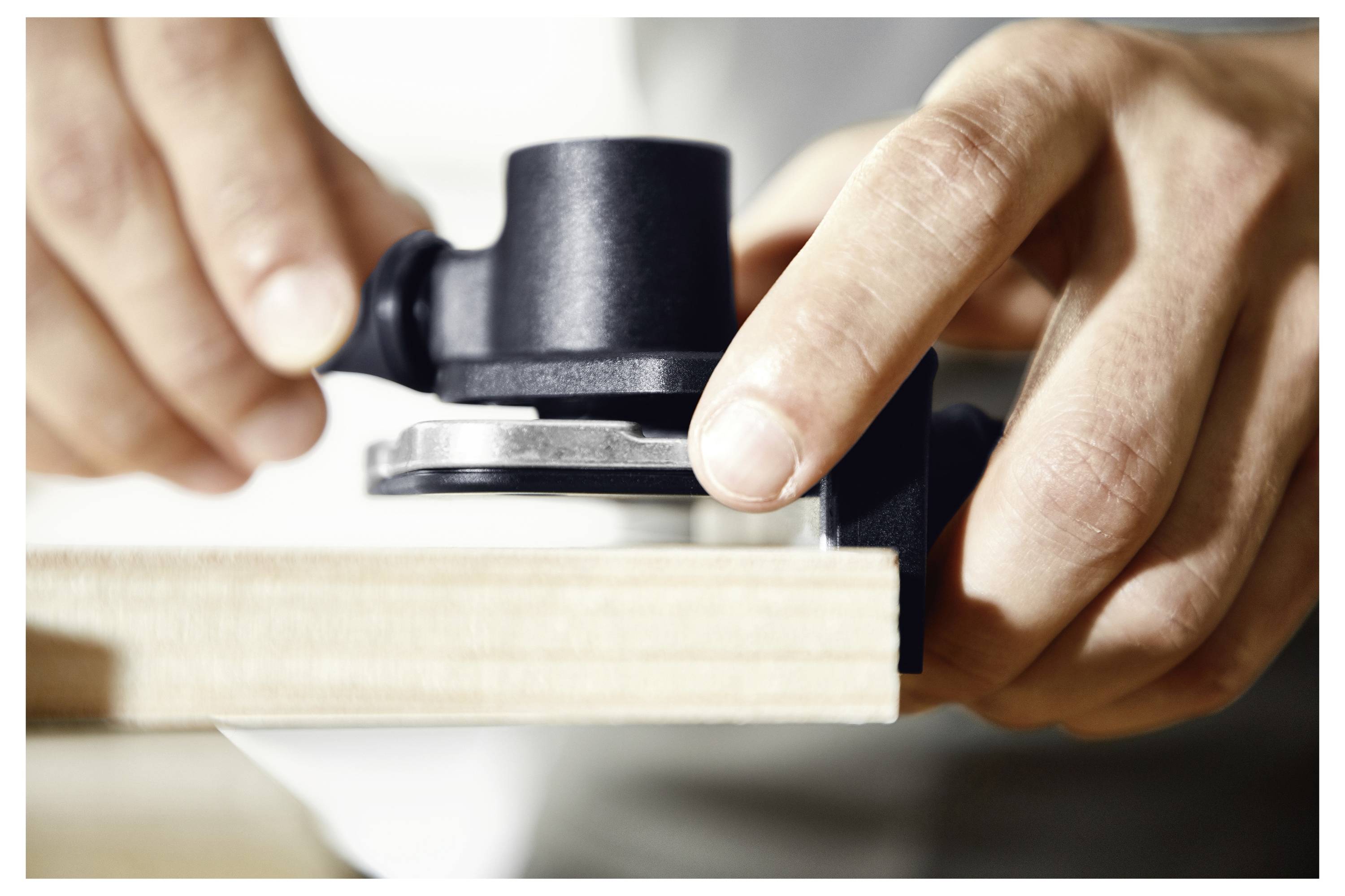 Eine Person verwendet ein schwarzes Scharniervorlagenwerkzeug an der Kante eines Holzbretts zum genauen Bohren und Einpassen.