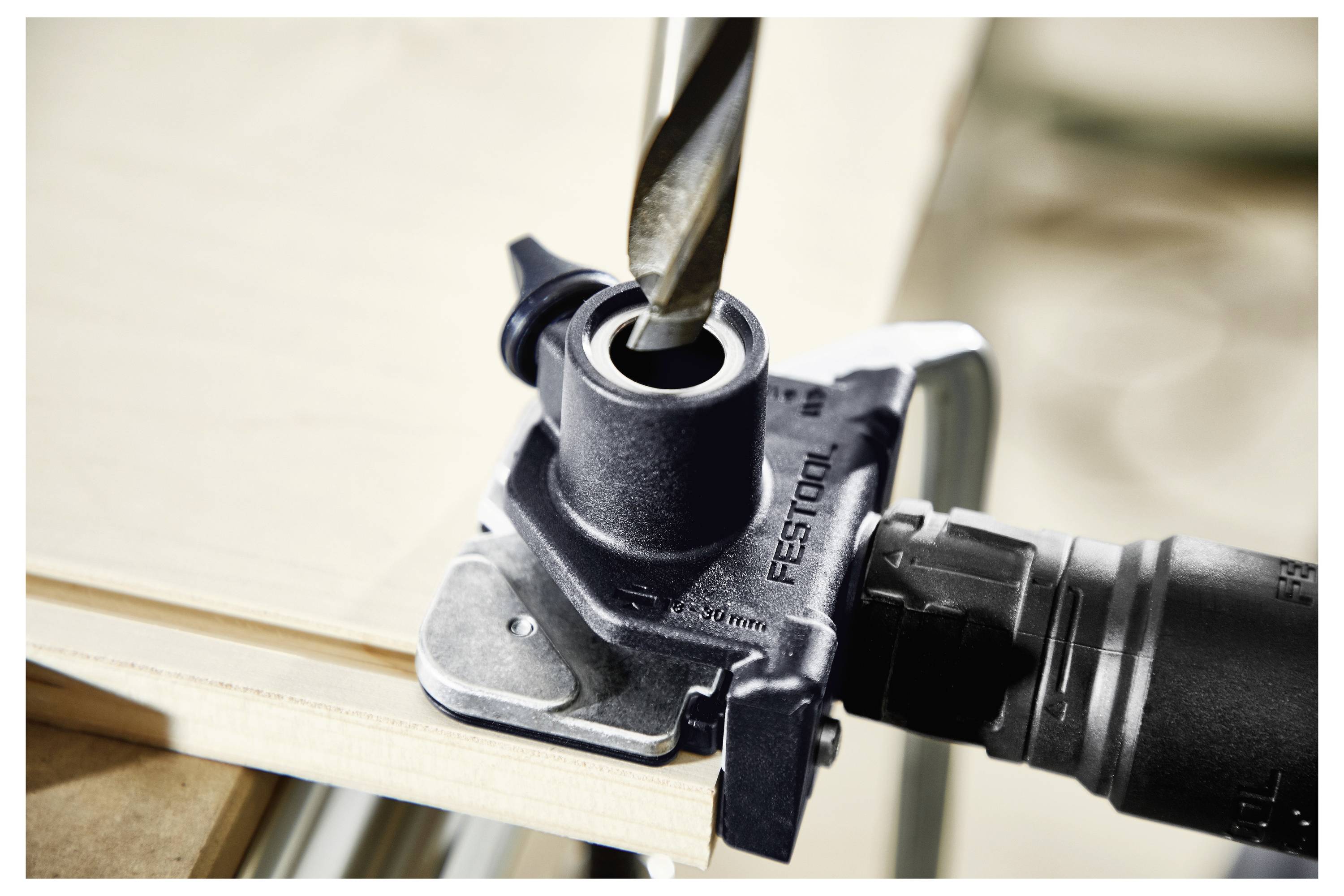A power drill is positioned at the edge of a wooden surface, fixed with a guide attachment for drilling precise holes.