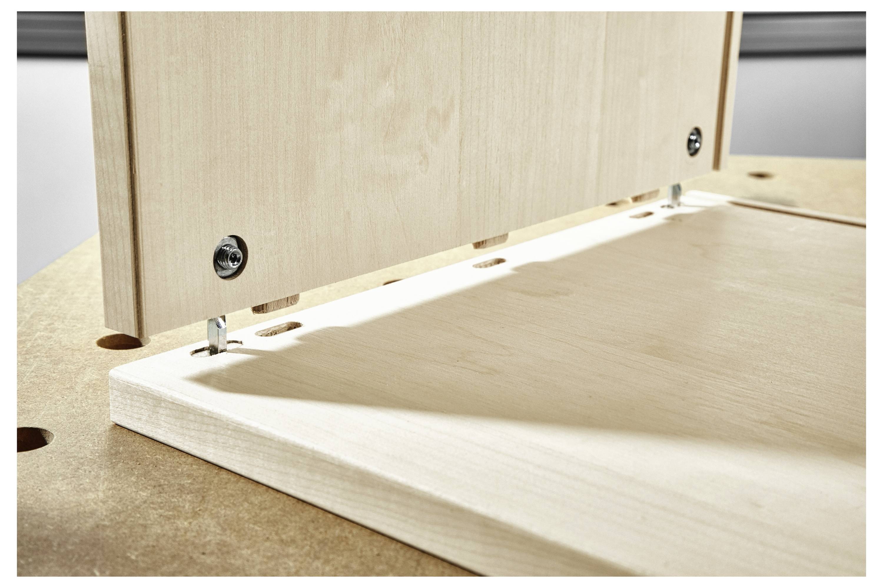 Close-up of two wooden panels being joined at a right angle with metal fasteners, demonstrating assembly technique on a table surface.