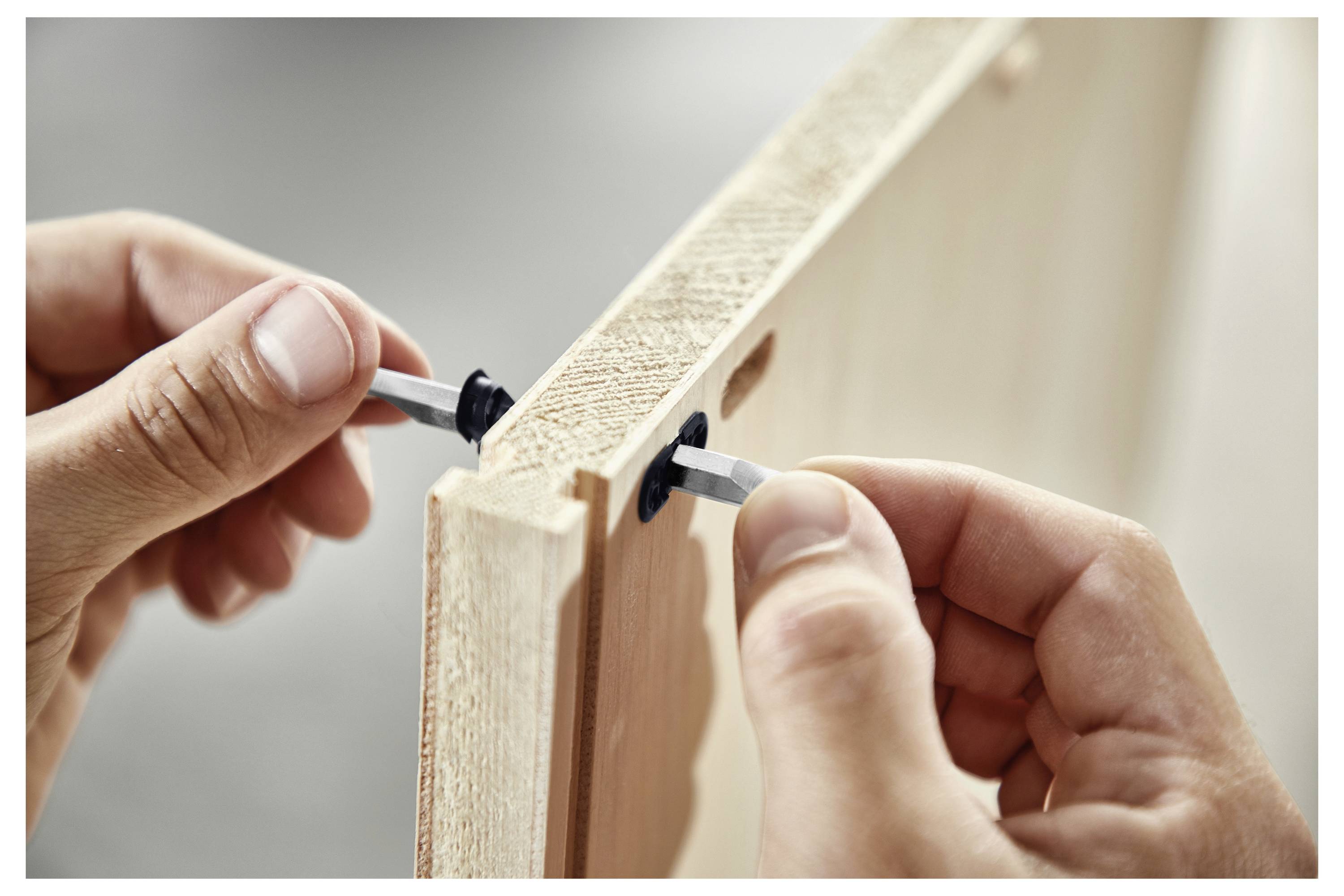 Zwei Hände montieren Möbel aus Holz mit Metallbefestigungen in einer Stoßkante-Verbindung und veranschaulichen den DIY-Möbelmontage-Prozess.