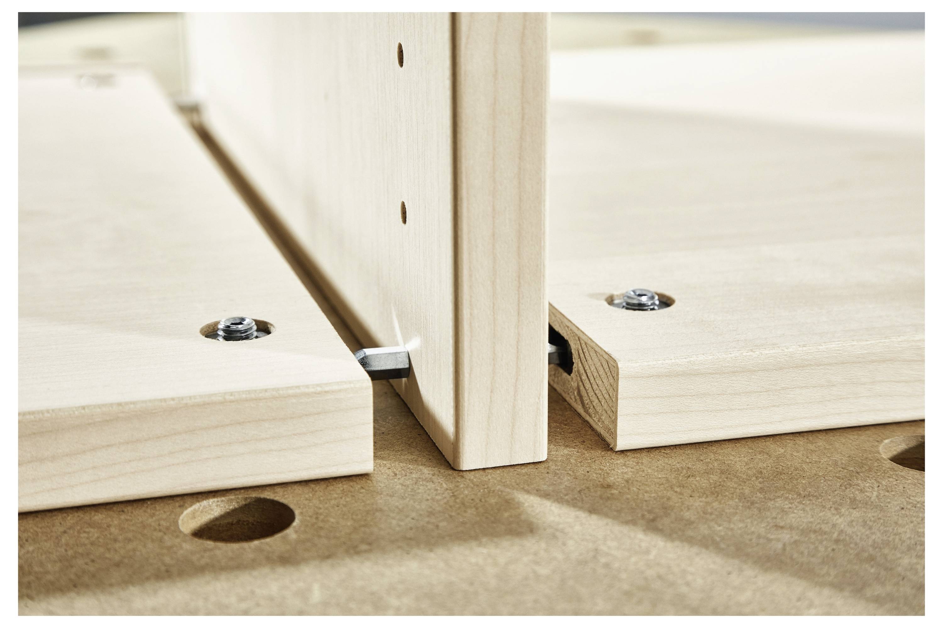 Nahaufnahme von zwei Teilen aus hellem Holz, die mit einem Dübel auf einer ebenen Fläche verbunden werden, zeigt die Ausrichtung und den Konstruktionsprozess.