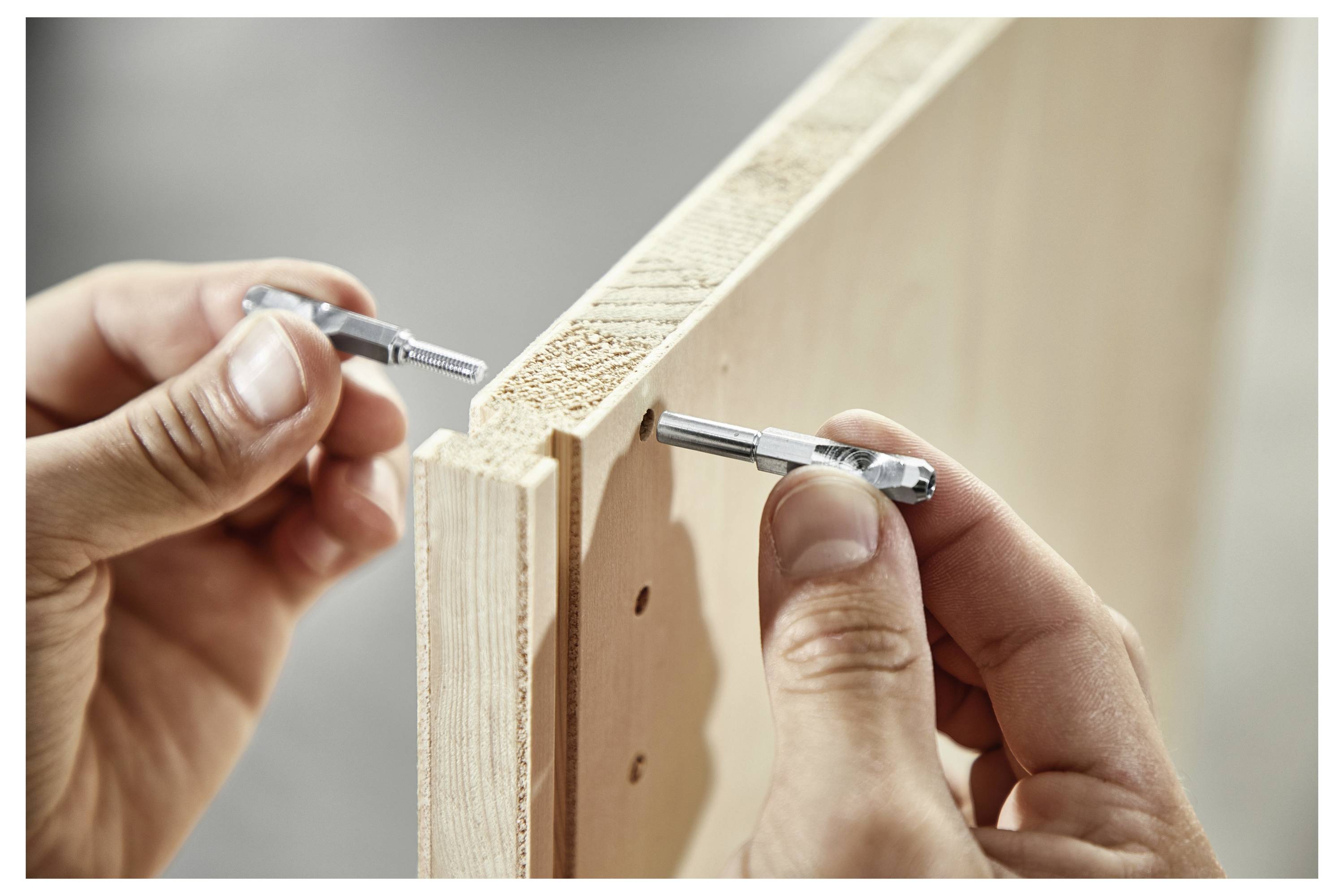 Eine Hand hält einen grün-schwarzen Elektrowerkzeug-Schlauchadapter, der mit einer Werkbank verbunden ist, und bereitet die Staubabsaugung während der Holzbearbeitung vor.