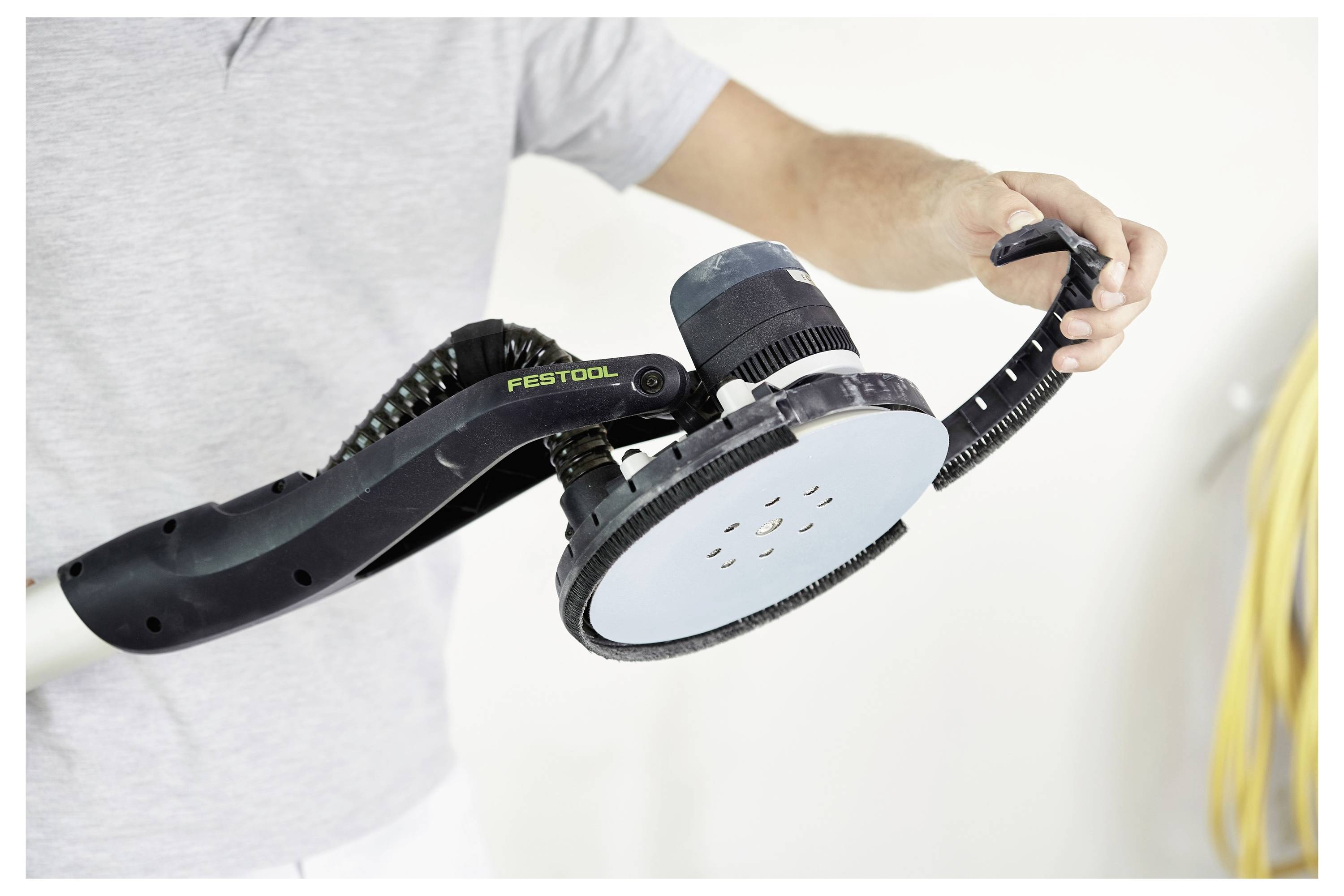 Eine Person hält einen elektrischen Schleifer der Marke Festool, wobei die kreisförmige Schleifscheibe hervorgehoben wird, mit Fokus auf das ergonomische Design des Werkzeugs.