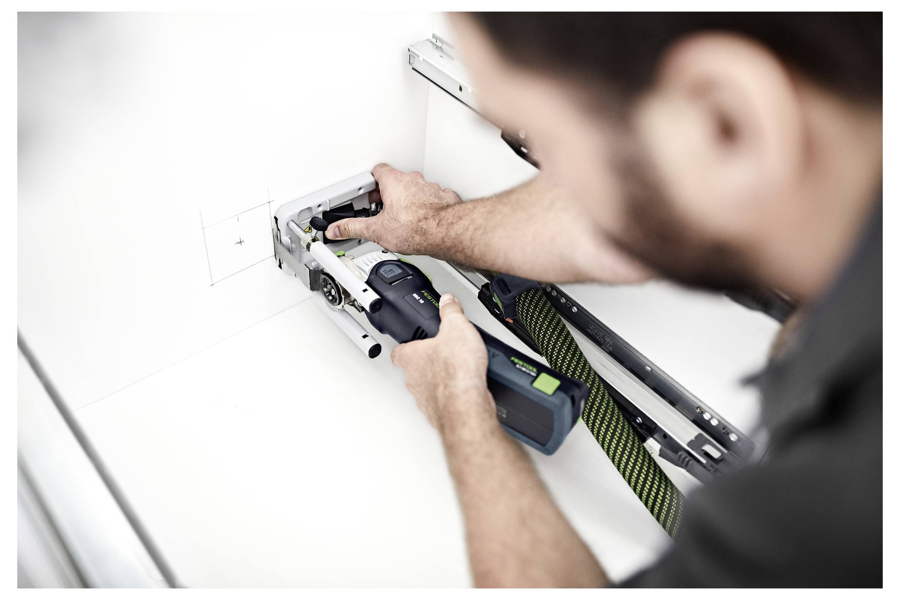 Eine Hand, die einen Festool-Schleiffer hält, glättet eine ebene Fläche und zeigt sein ergonomisches Design und seine Funktionalität in einer Werkstattumgebung.