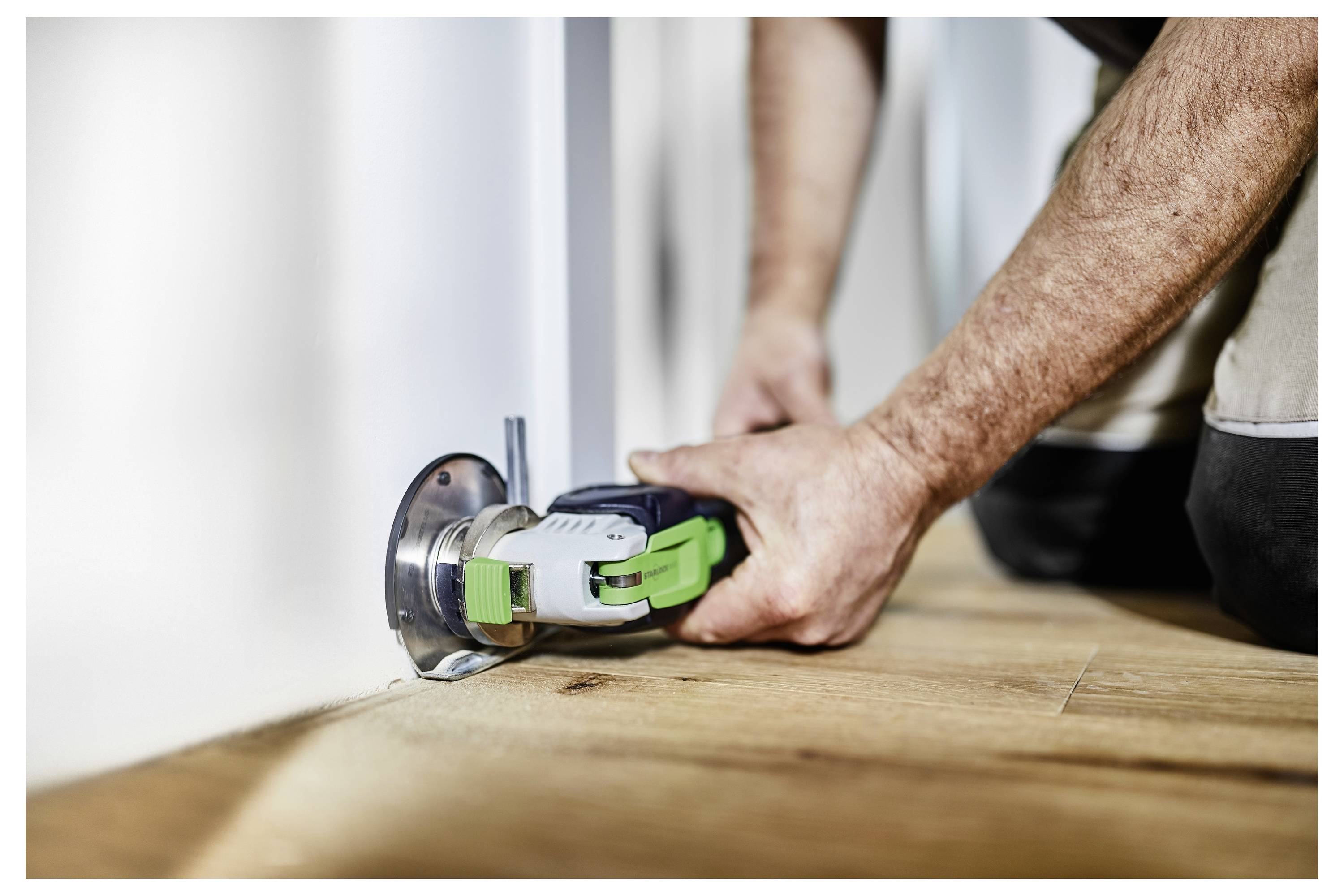A person using a power tool to cut flooring near a wall, demonstrating precision in home renovation or construction work.