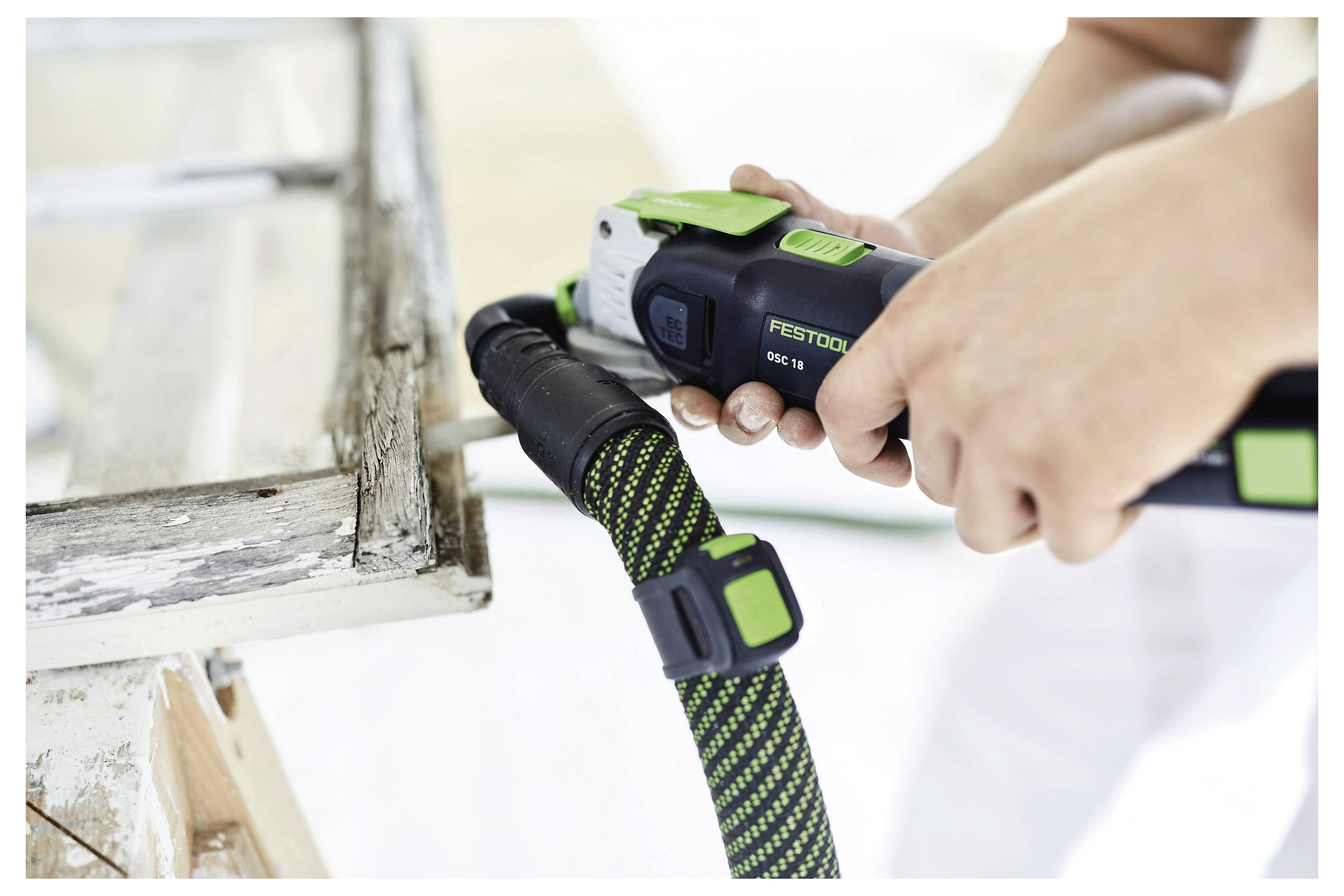 Eine Person benutzt ein Elektrowerkzeug mit grünem und schwarzem Design zum Schleifen oder Polieren eines Möbelstücks aus Holz, wobei der Fokus auf dem Werkzeug und der Handlung liegt.