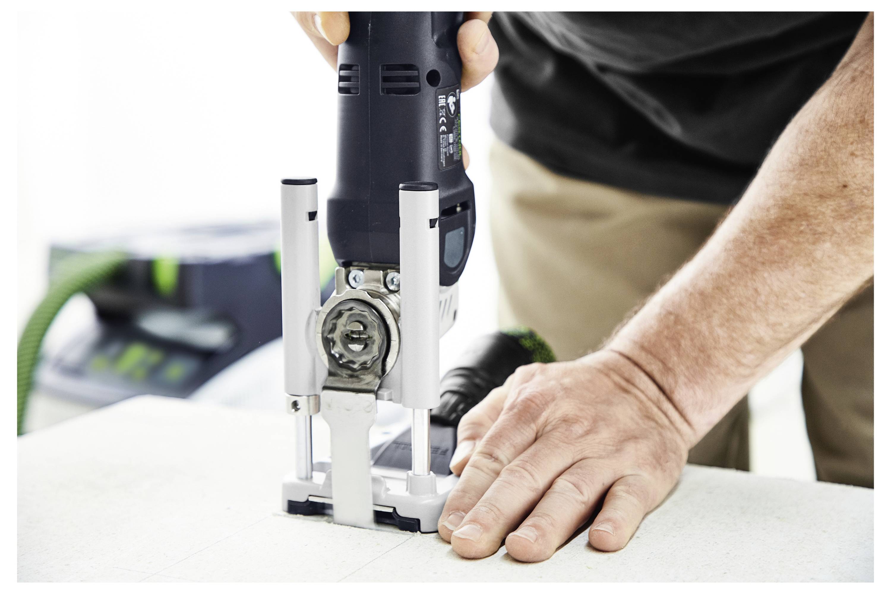 A person using a power tool to rout the edge of a light-colored surface, with focus on the hands and tool operation.