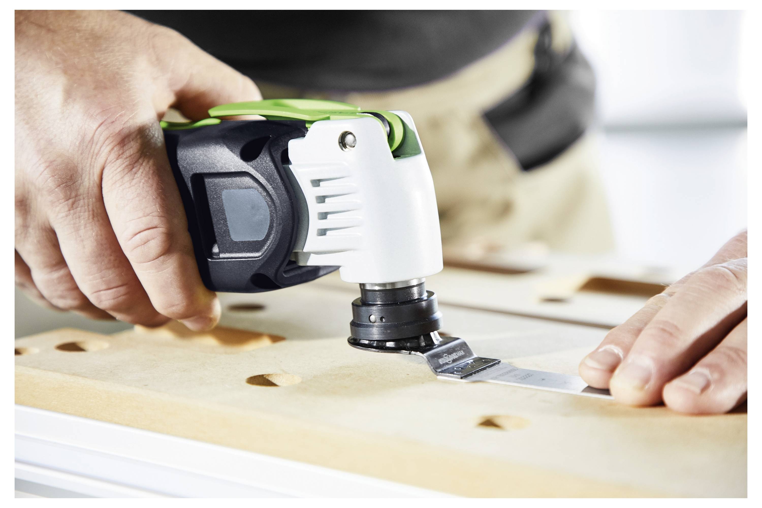 A person uses an oscillating multi-tool to cut into a wooden surface, focusing on precision and control in a workshop setting.