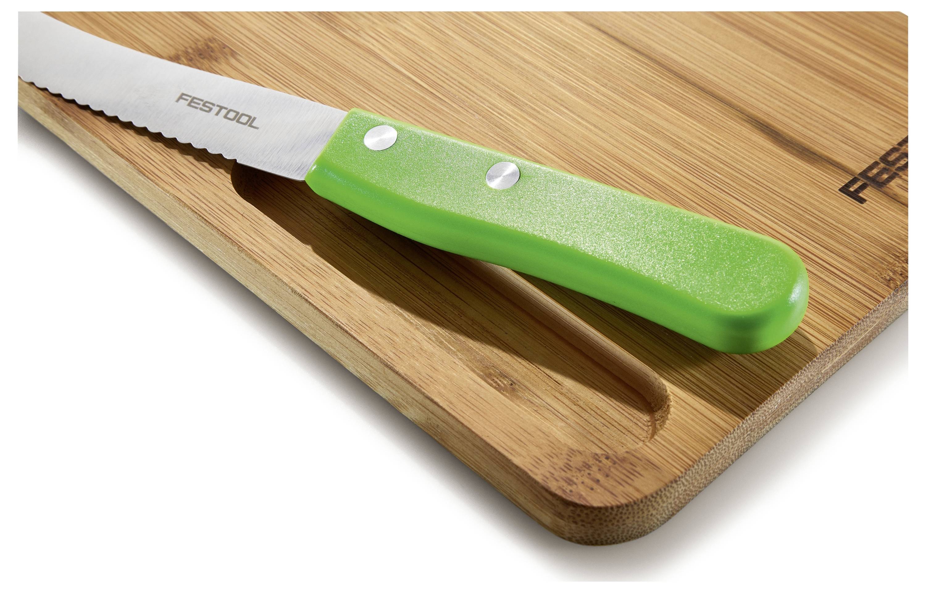 Ein Messer mit Wellenschliff und grünem Griff ruht auf einem Bambusschneidebrett mit 
