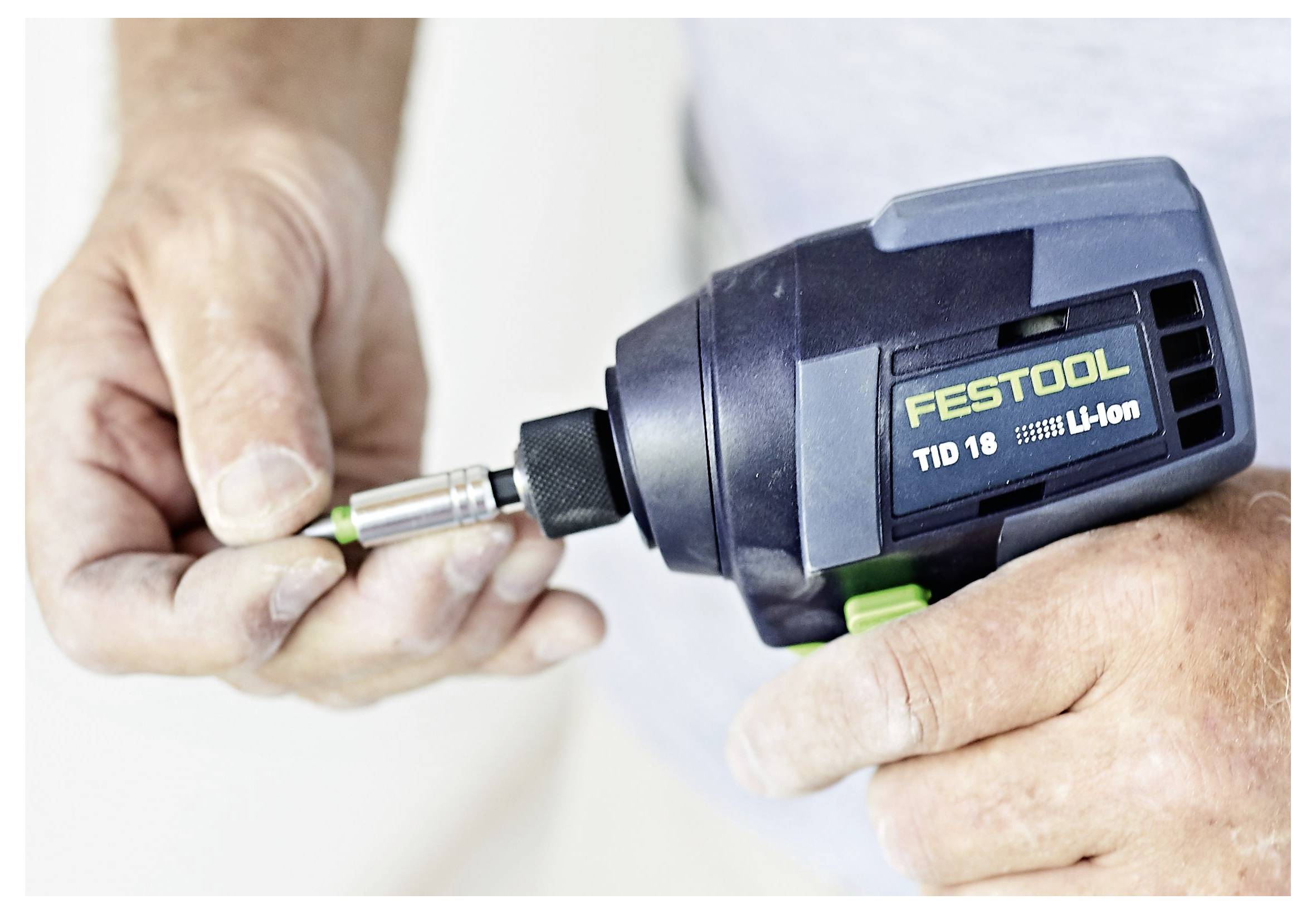 Eine Person führt einen Aufsatz in eine Festool TID 18 Li-Ion Akku-Bohrmaschine ein, Nahaufnahme von Händen und der Bohrmaschine.