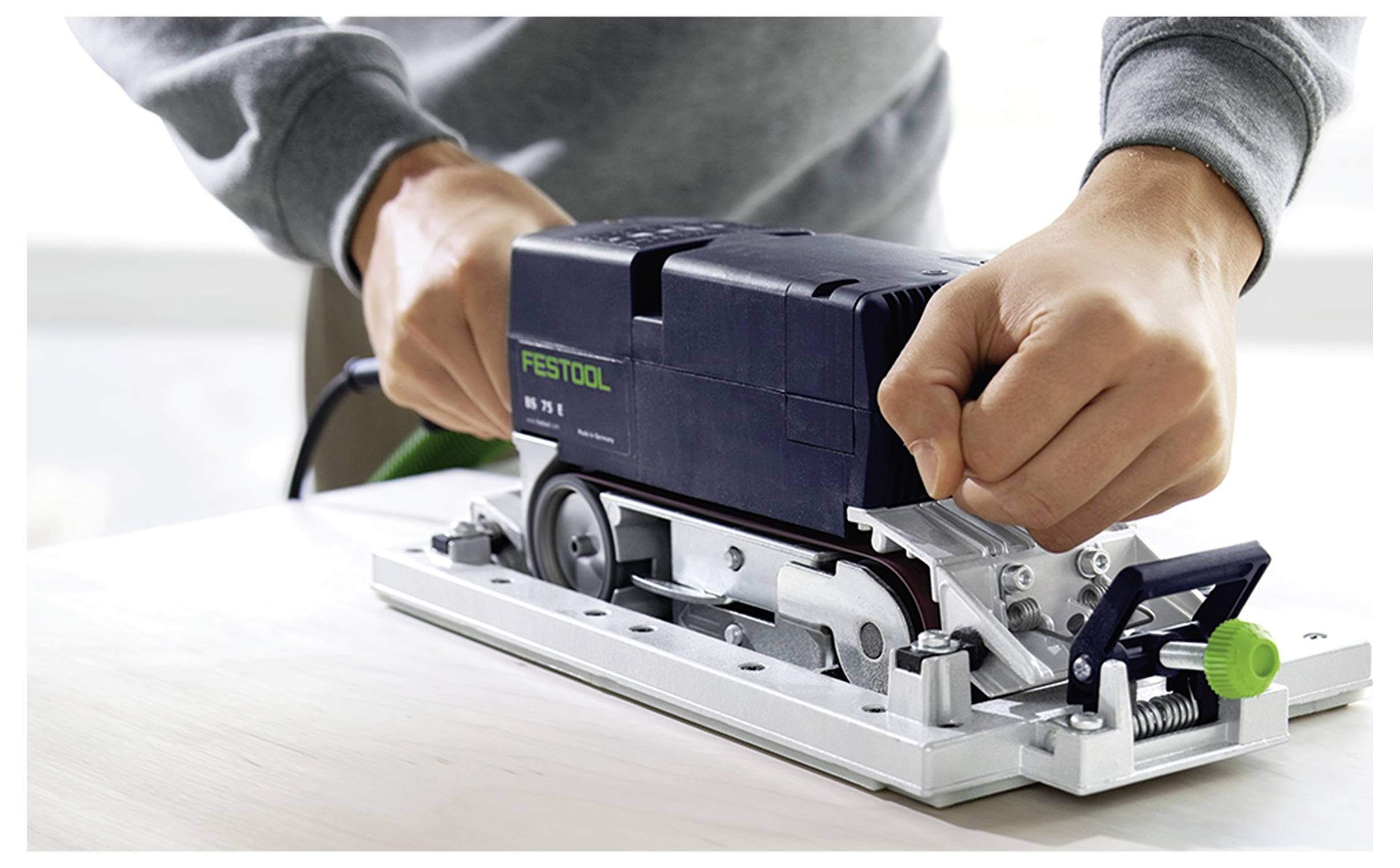 Eine Person benutzt einen tragbaren elektrischen Schleiffer auf einer Autoberfläche und trägt Handschuhe zum Schutz. Die Szene unterstreicht Autowerkstatt-Reparaturarbeiten.