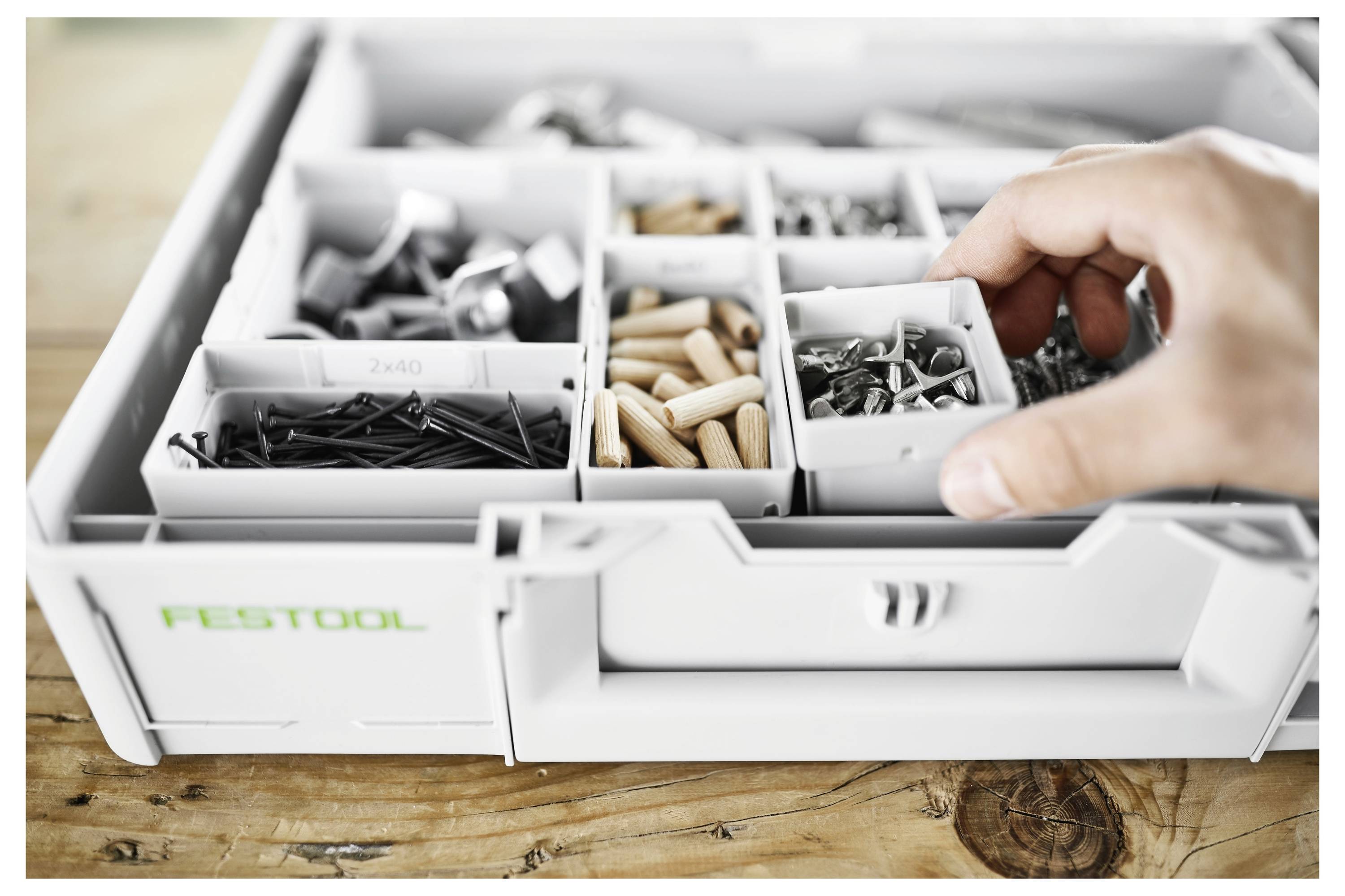 Eine Aufbewahrungsbox mit mehreren Fächern, die verschiedene Schrauben, Nägel und Dübel enthält, wird geöffnet. Eine Hand nimmt ein kleines Teil heraus.