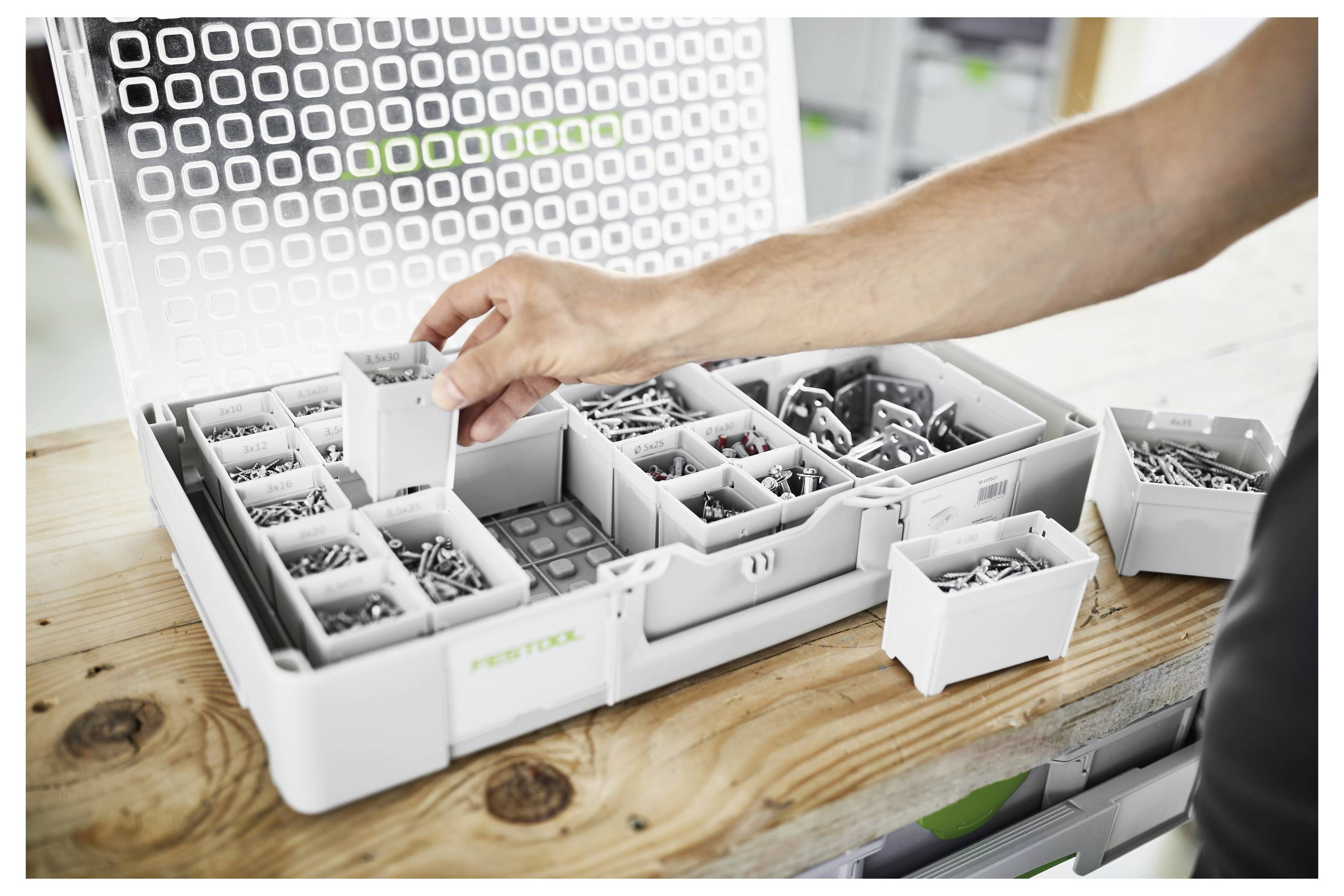 Eine offene Werkzeugkiste mit einer Hand, die Schrauben aus einer unterteilten Box auswählt, was die Organisation und Zugänglichkeit von Hardware-Teilen verdeutlicht.