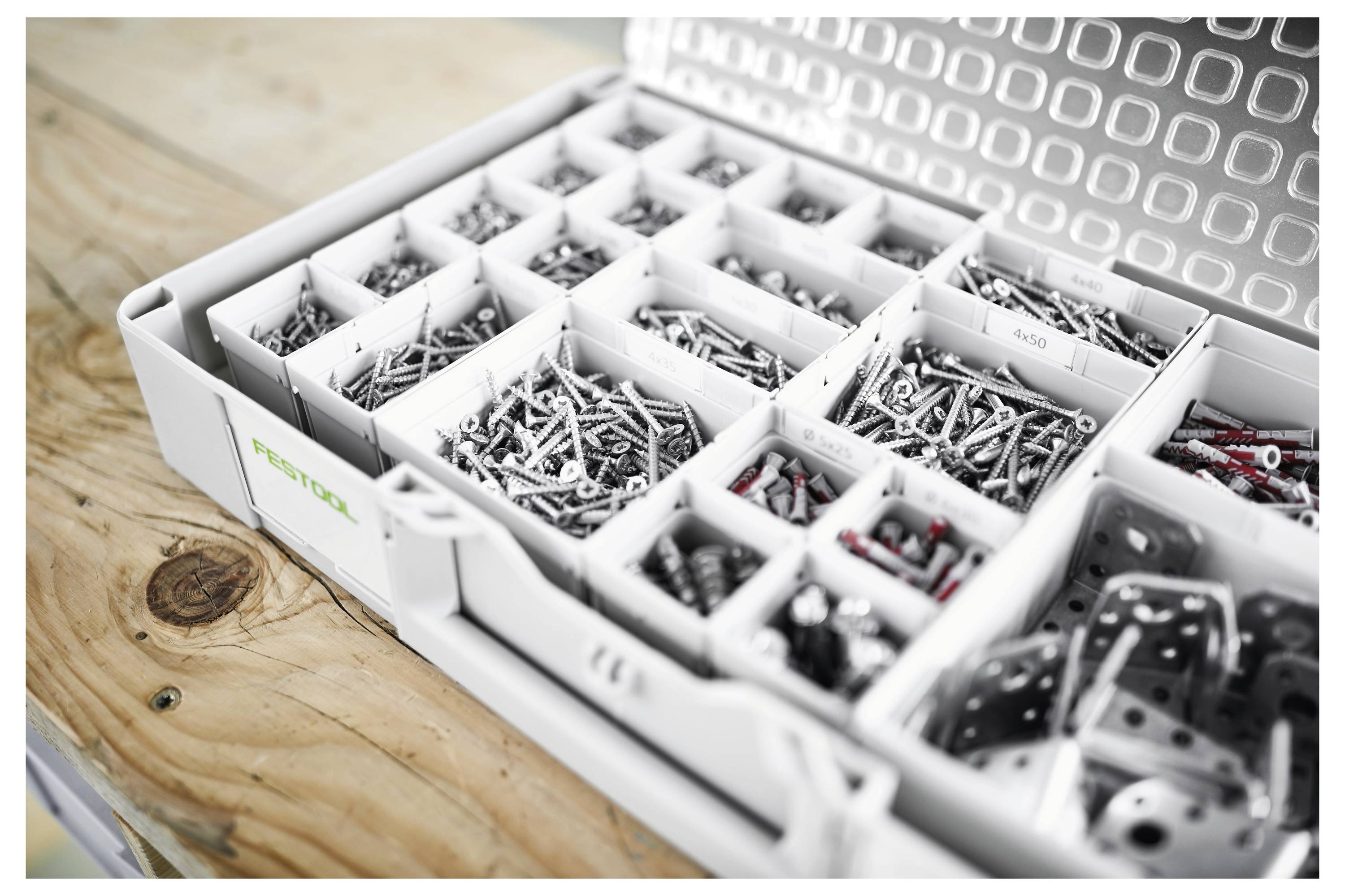 Eine offene Organisationsbox auf einer Holzoberfläche, gefüllt mit sortierten Schrauben, Muttern und Bolzen, ordentlich in beschrifteten Fächern angeordnet.