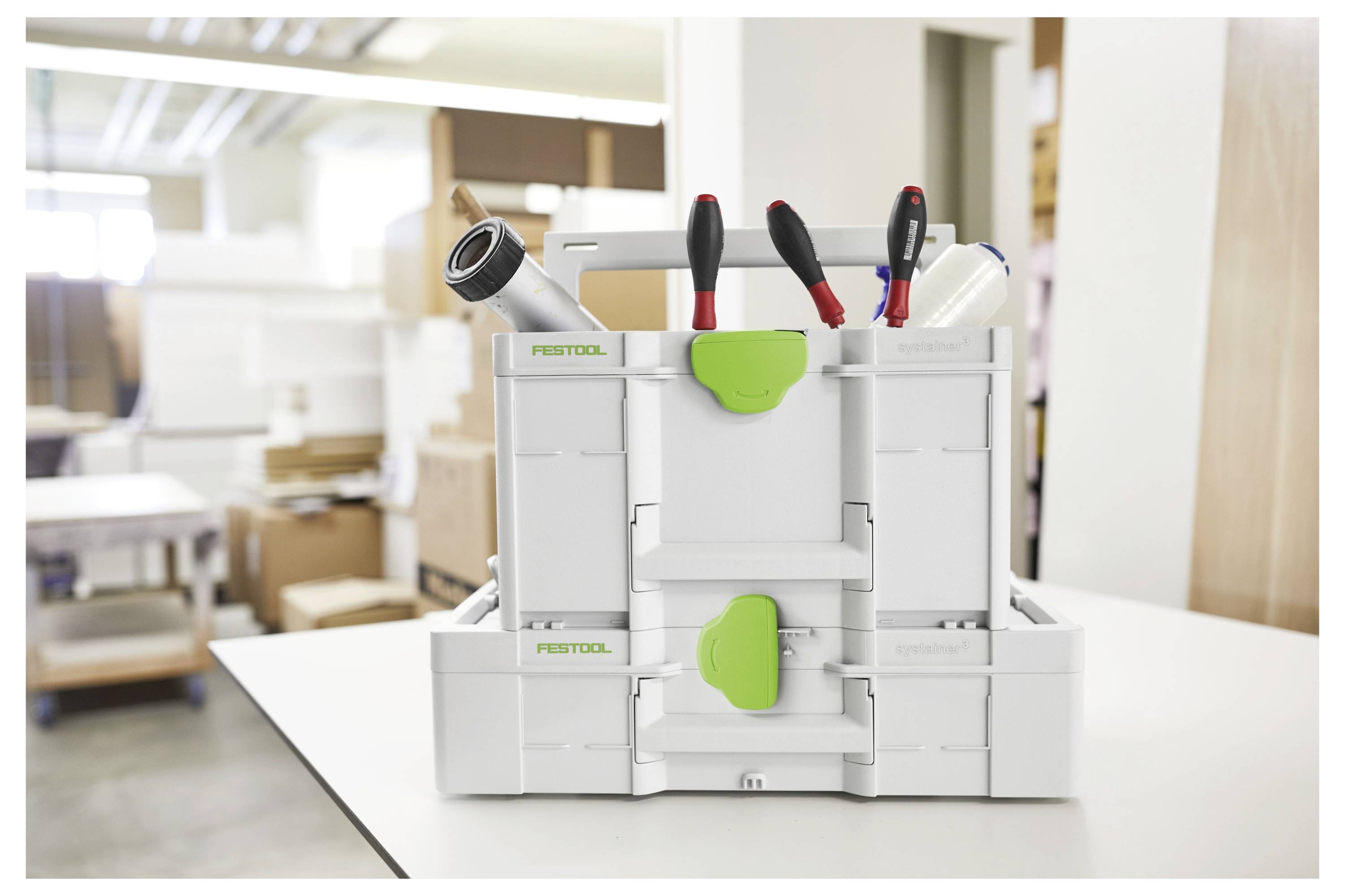 Eine Werkzeugkiste mit verschiedenen Werkzeugen, einschließlich Zangen und Schraubendrehern, steht auf einem Tisch in einer Werkstattumgebung.