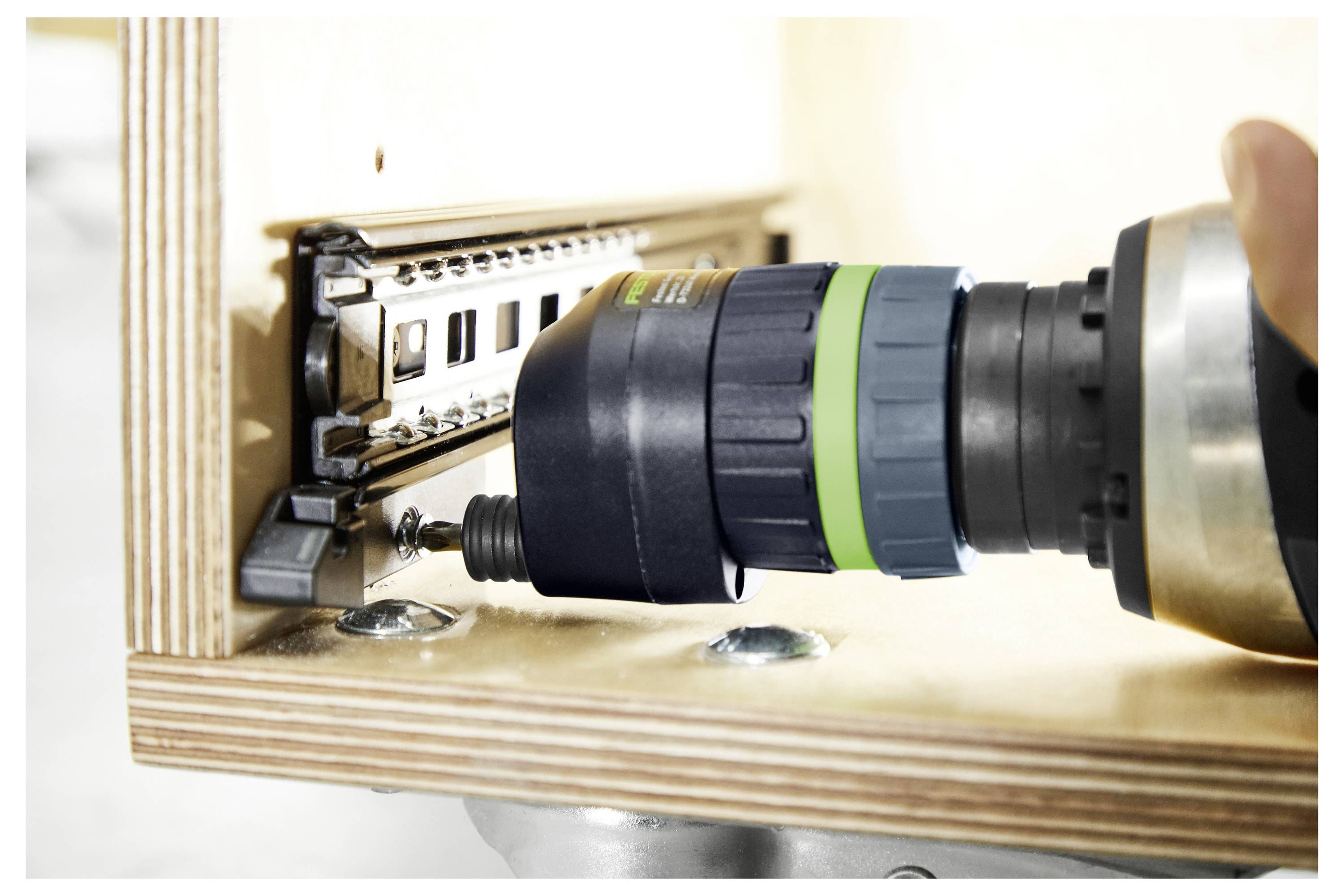 Eine Person benutzt Holzbearbeitungsmaschinen in einer hellen Werkstatt, mit Fokus auf eine Festool-Absauganlage im Vordergrund.