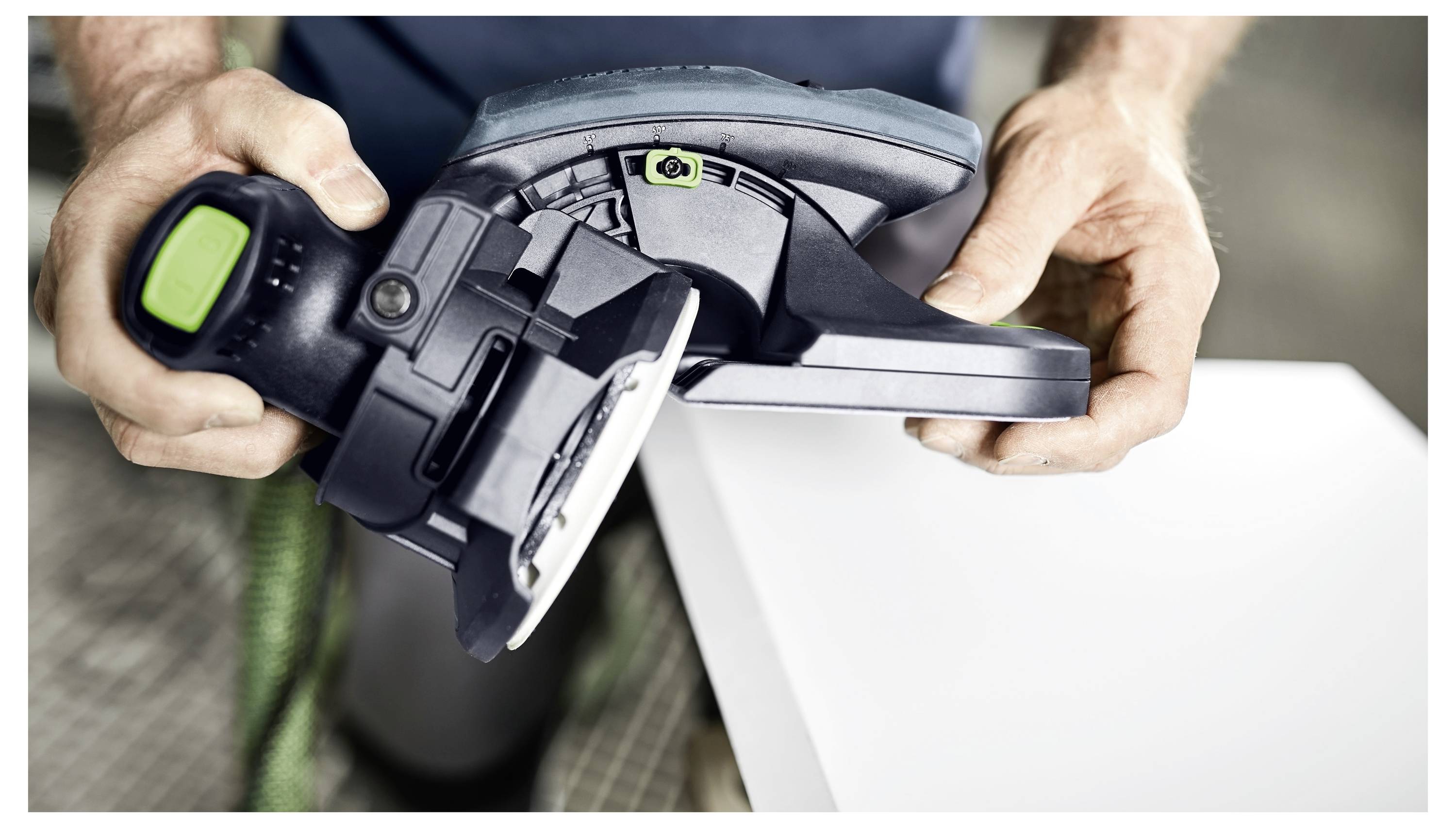 Eine Person, die ein Elektrowerkzeug auf einer weißen Oberfläche verwendet, wobei der Fokus auf den Händen und dem Werkzeug liegt.