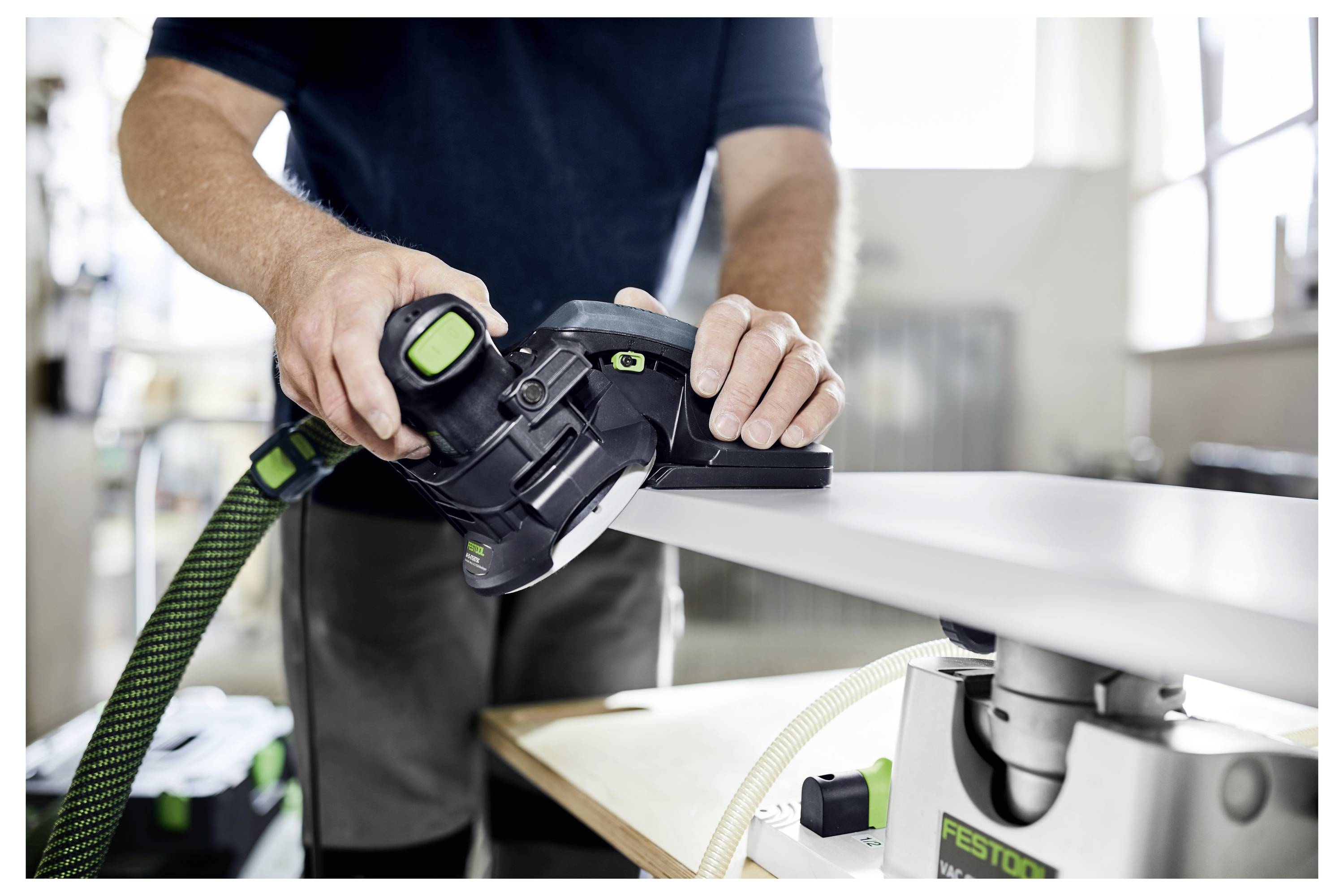 Eine Person verwendet ein Festool-Elektrowerkzeug zum Glätten der Kante eines Holzbretts in einer Werkstatt und unterstreicht dabei Präzision und handwerkliches Geschick.