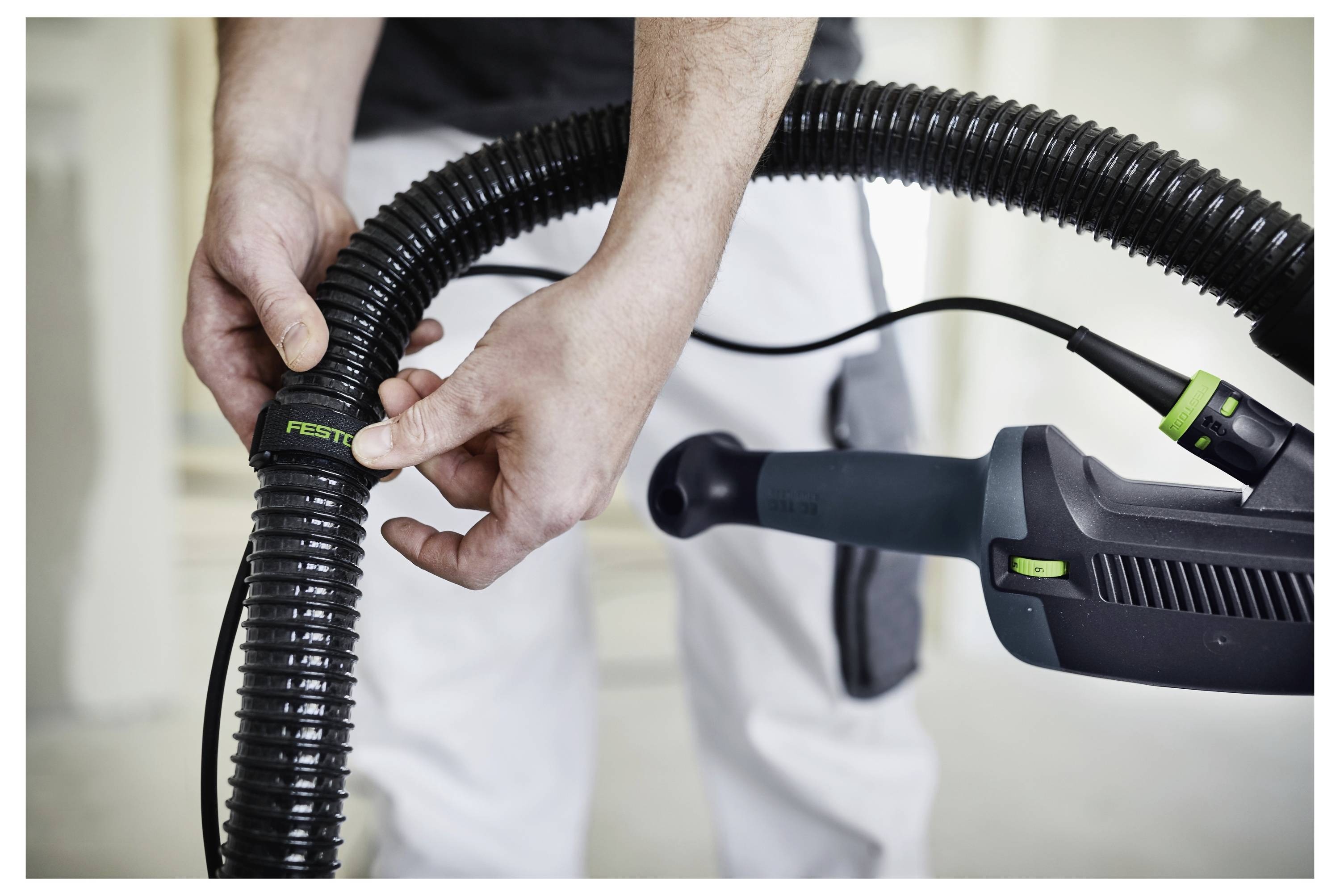 Eine Person befestigt einen Schlauch der Marke Festool an einem Werkzeug und demonstriert damit die Ausrüstungseinstellung für Bau- oder Heimwerkerarbeiten.