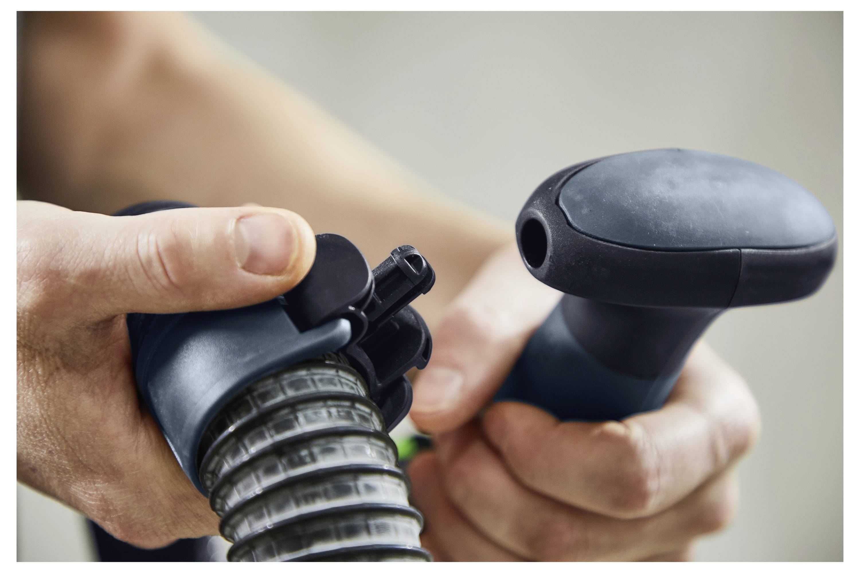 Hände, die einen flexiblen Schlauch und eine Düsenaufsatz halten und zusammensetzen, wobei der Fokus auf dem Verbindungsmechanismus liegt, geeignet für Vakuum- oder Reinigungsgeräte.