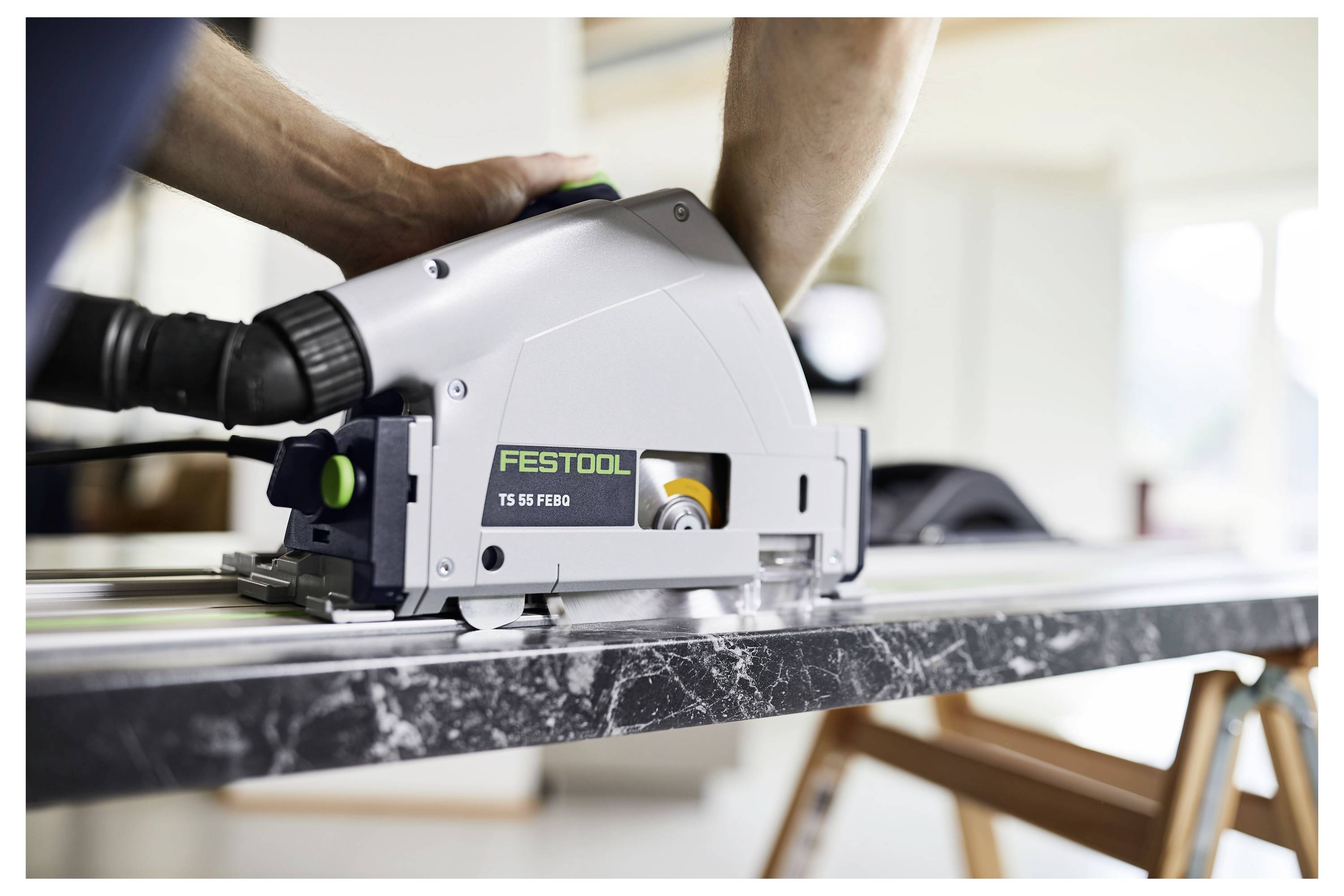 Eine Person benutzt eine Festool TS 55 FEBQ Kreissäge, um ein Stück dunklen Marmor auf einer Werkbank zu schneiden.