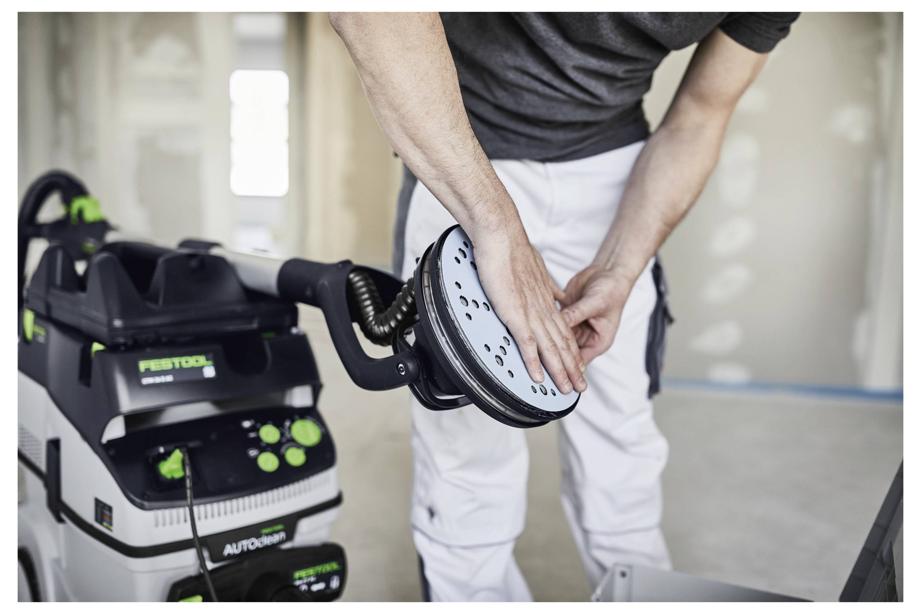 Die Hand einer Person bedient einen Festool ETSC 125 Akku-Schleifer auf einer hellen Oberfläche, wobei sein kompaktes Design und seine Benutzerfreundlichkeit demonstriert werden.