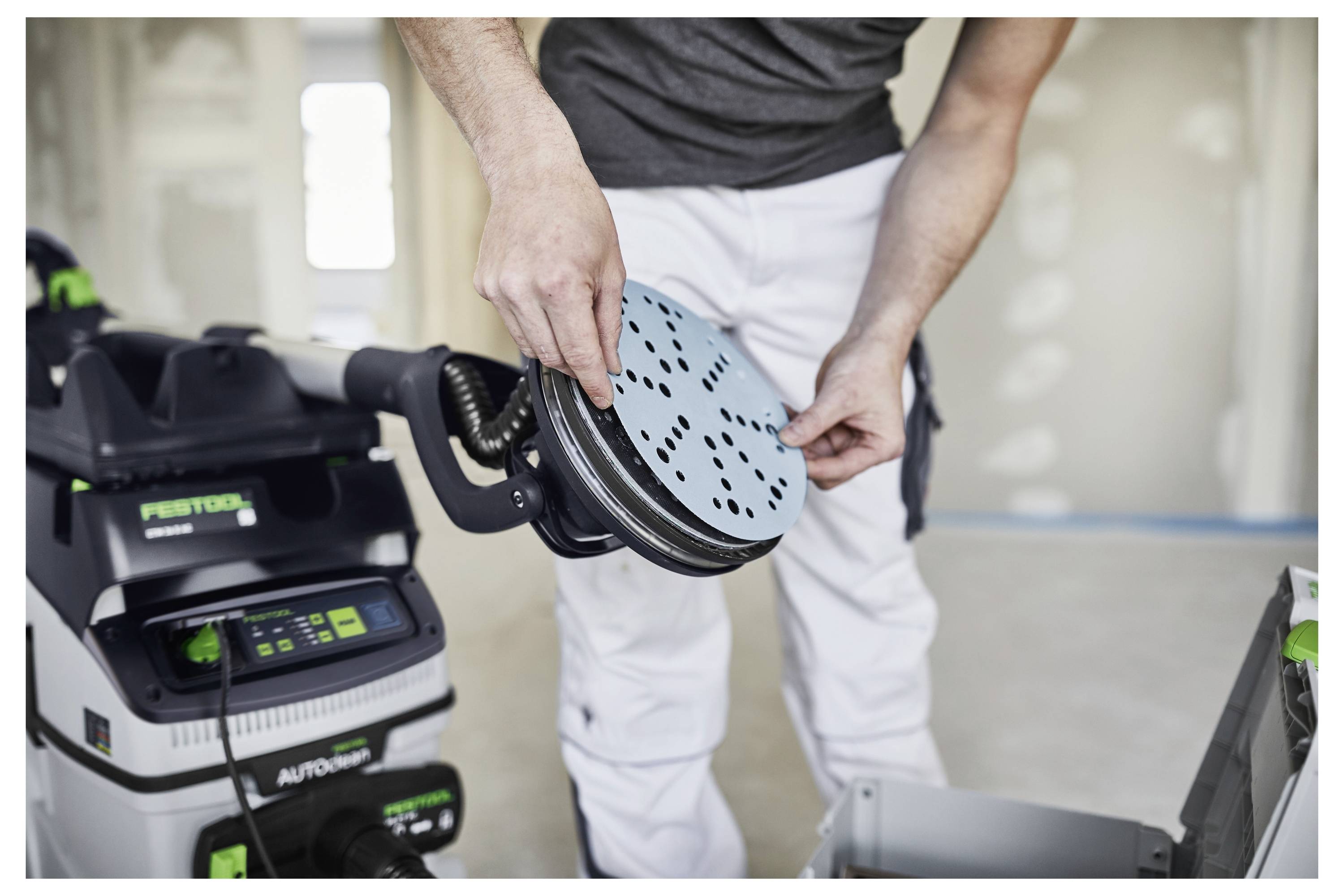 Eine Person befestigt eine Schleifscheibe auf einem Elektrowerkzeug in einer Baustelle und bereitet sich darauf vor, Oberflächen zu schleifen.