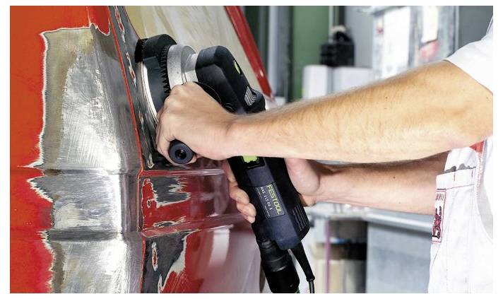 Person, die einen Elektroschleiffer auf einer roten Metalloberfläche in einer Werkstattumgebung verwendet, um die Kanten für eine verfeinerte Oberflächenbehandlung zu glätten.