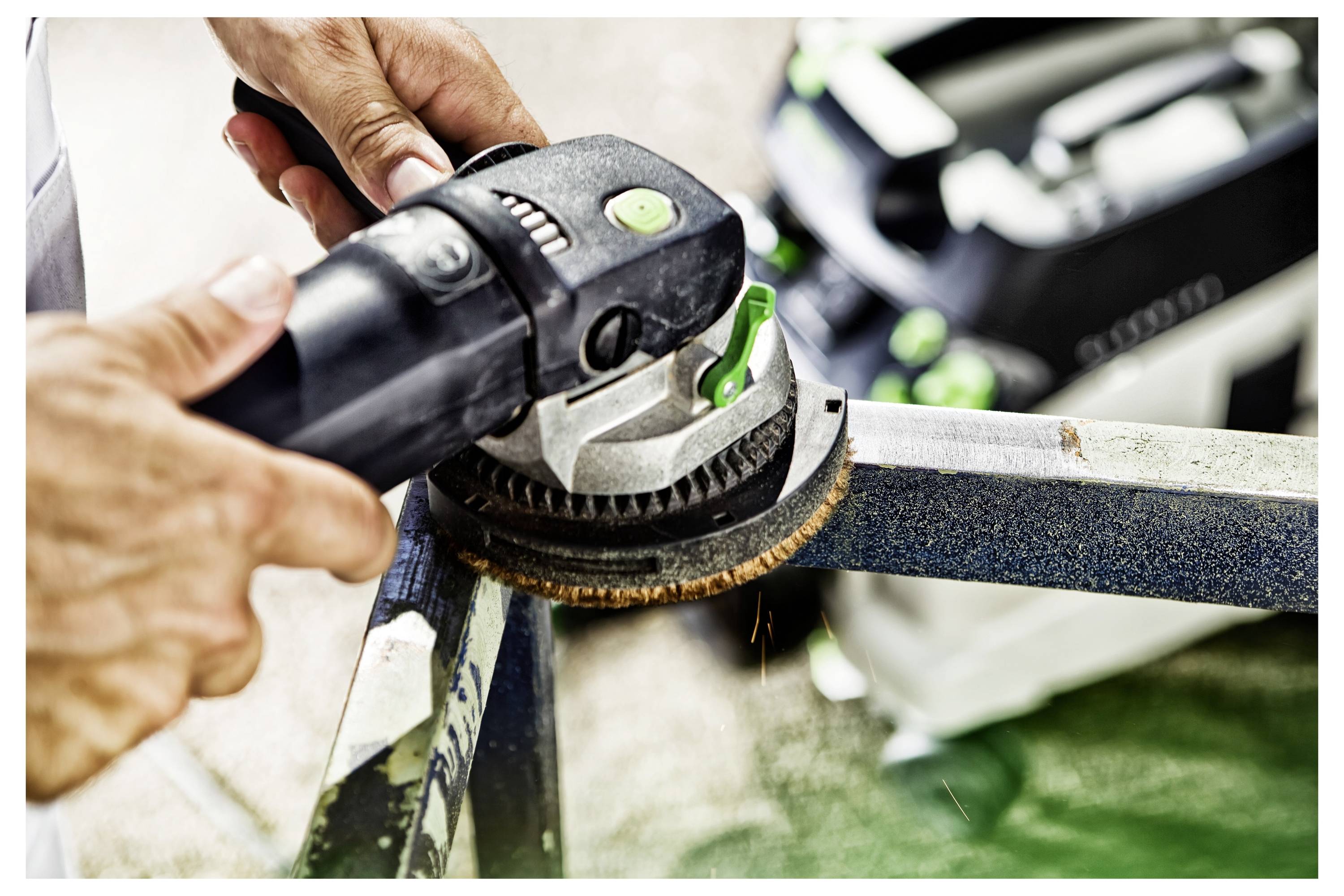 Eine Person verwendet einen elektrischen Schleifer auf einer Metalloberfläche und erzeugt dabei Funken. Der Schleifer hat einen schwarzen Griff und grüne Akzente.