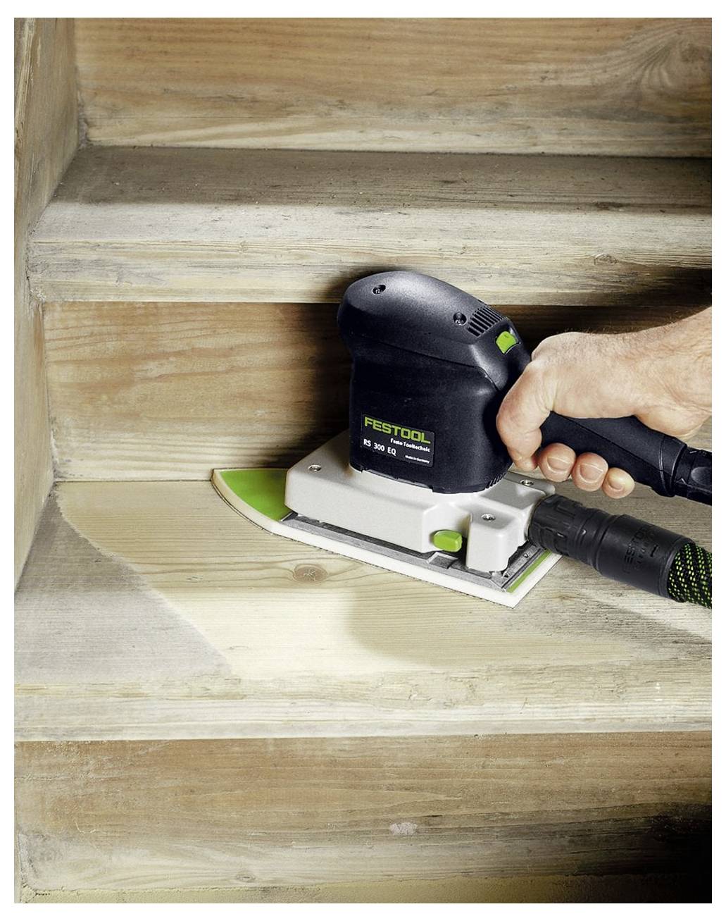 Eine Hand benutzt einen elektrischen Schleiffer, um eine Holztreppe zu glätten und zu überarbeiten, wobei die oberste Schicht entfernt wird, um das darunter liegende saubere Holz freizulegen.