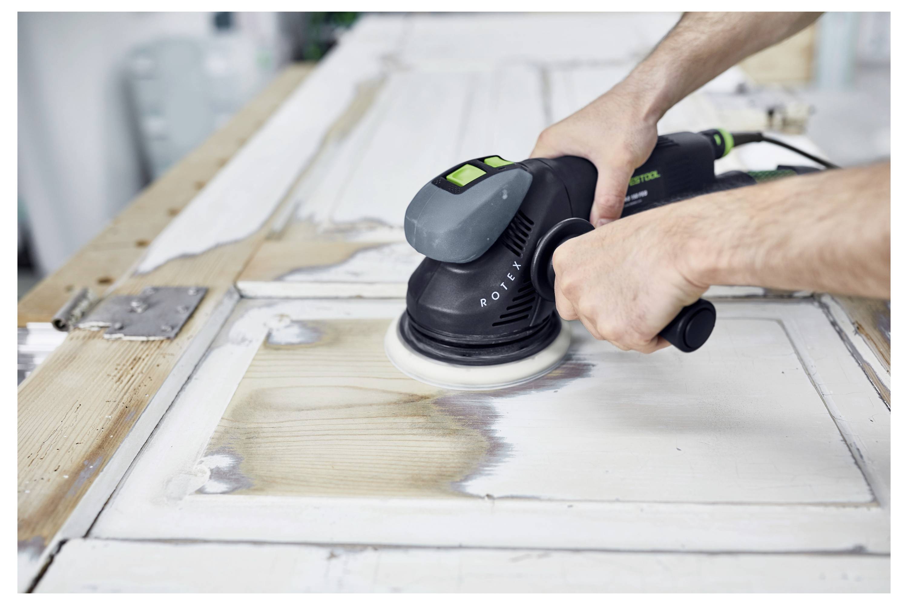 Eine Person mit Schutzbrille und Maske benutzt einen Elektroschleiffer an einer Wand, was auf eine Hausrenovierung oder Bautätigkeit hinweist.