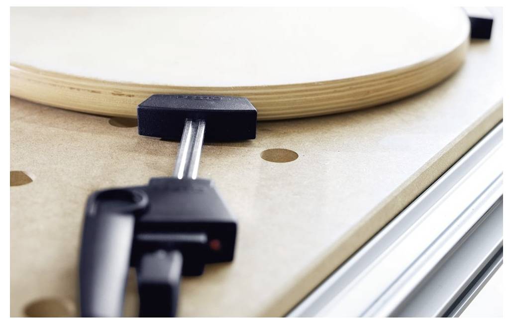 Eine Holzbearbeitungszwinge sichert ein kreisförmiges Holzstück auf einer Werkbank mit glatter Oberfläche und gleichmäßig verteilten Löchern.