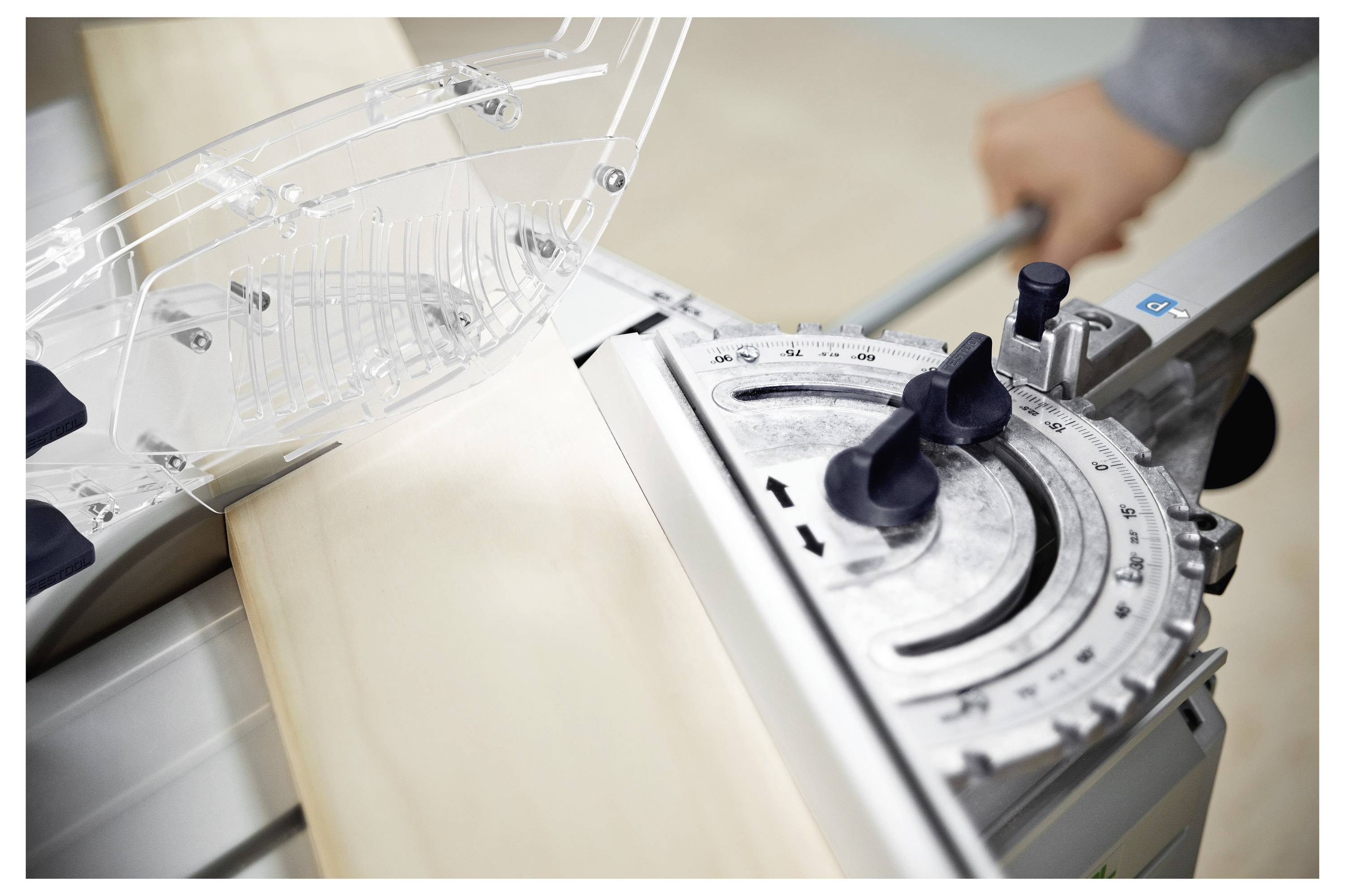 Ein Holzarbeiter nutzt eine Schraubzwinge, um ein Holzstück in einer Werkstatt fest zu halten, während Werkzeuge und der Arbeitsbereich im Hintergrund verschwommen sind.