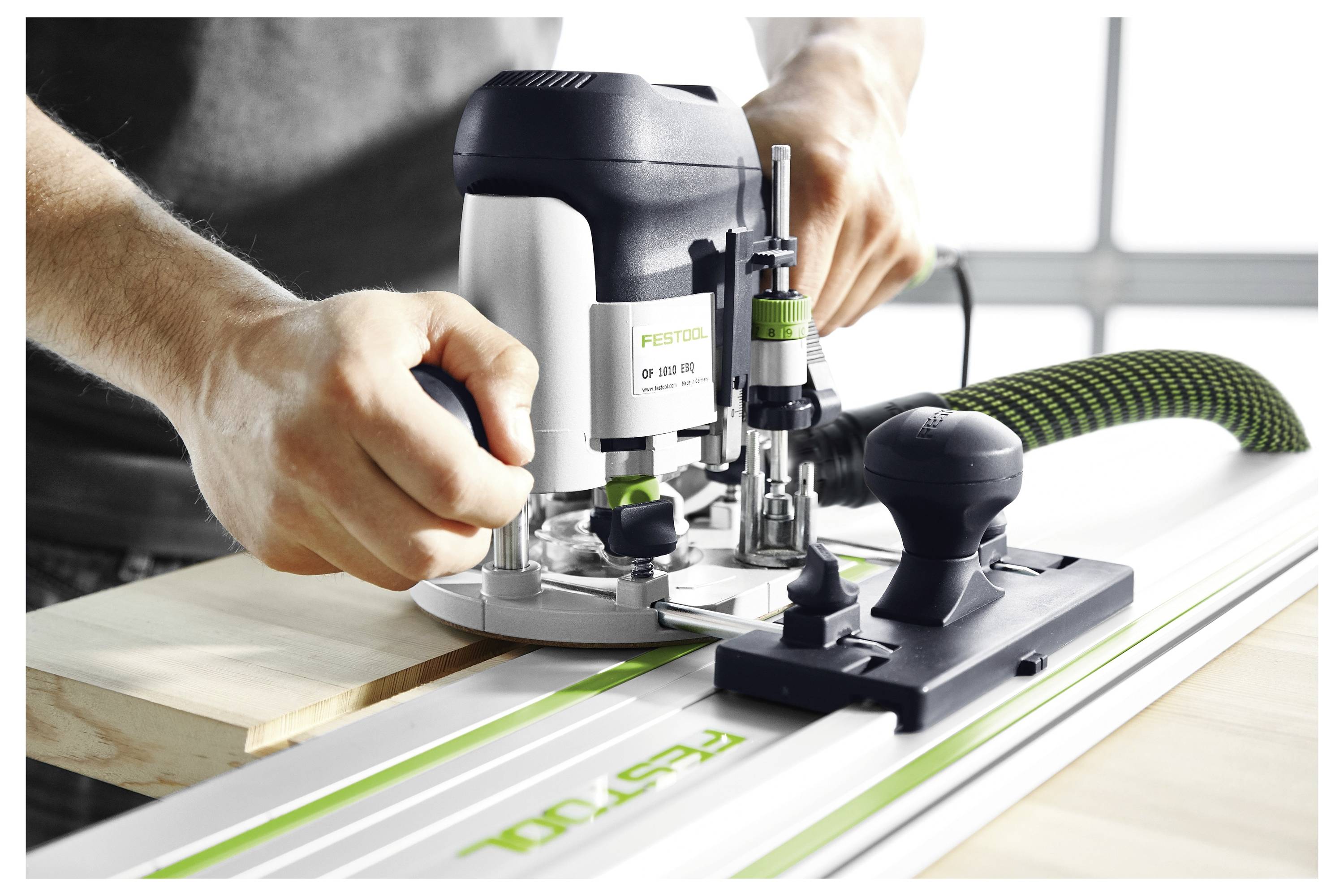 Eine Person bedient eine Festool-Fräsmaschine auf einem Führungsschienensystem und demonstriert präzise Holzbearbeitung mit Fokus auf Werkzeughandhabung und Ausrichtung.