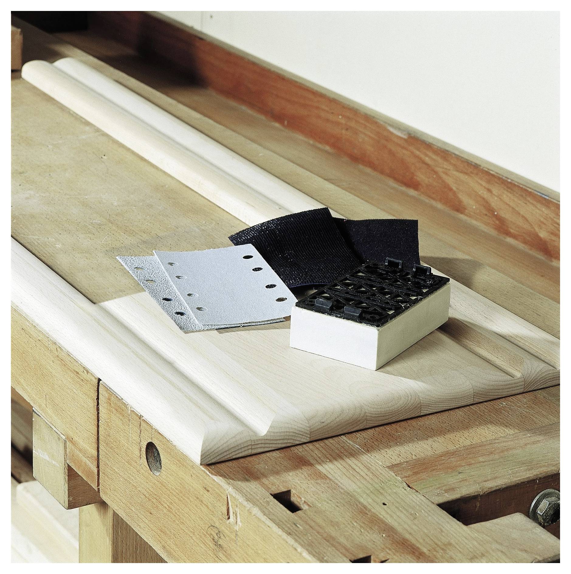 Holzbearbeitungswerkzeuge und Materialien auf einer Werkbank, einschließlich Schleifpapier, einem Schleifblock und Holzleisten, bereit zum Handwerk.