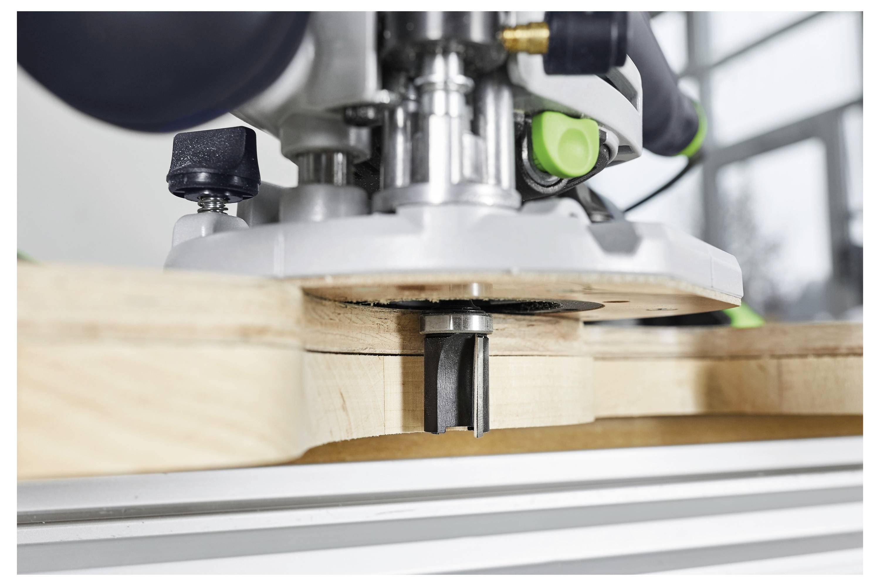 Eine Nahaufnahme einer Holzfräsmaschine, die eine Nut in ein Holzbrett fräst, mit Fokus auf den Metallfräser und die Präzision der Maschine.
