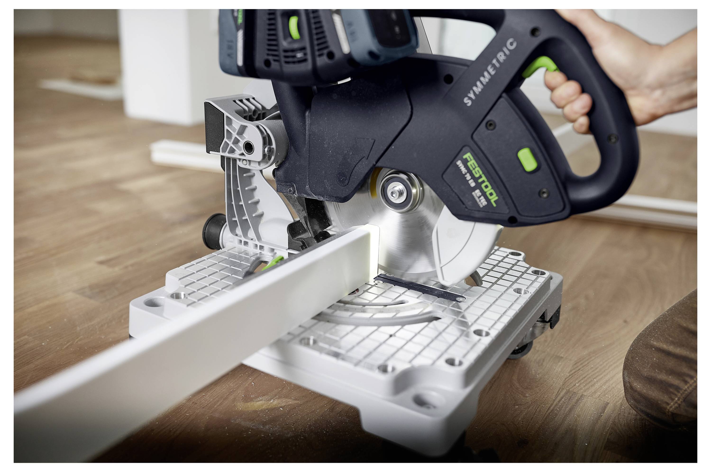 Eine Person benutzt eine Elektro-Gehrungssäge, um ein Stück Holz auf einer Werkbank zu schneiden, mit dem Fokus auf das Sägeblatt und das Holzstück.