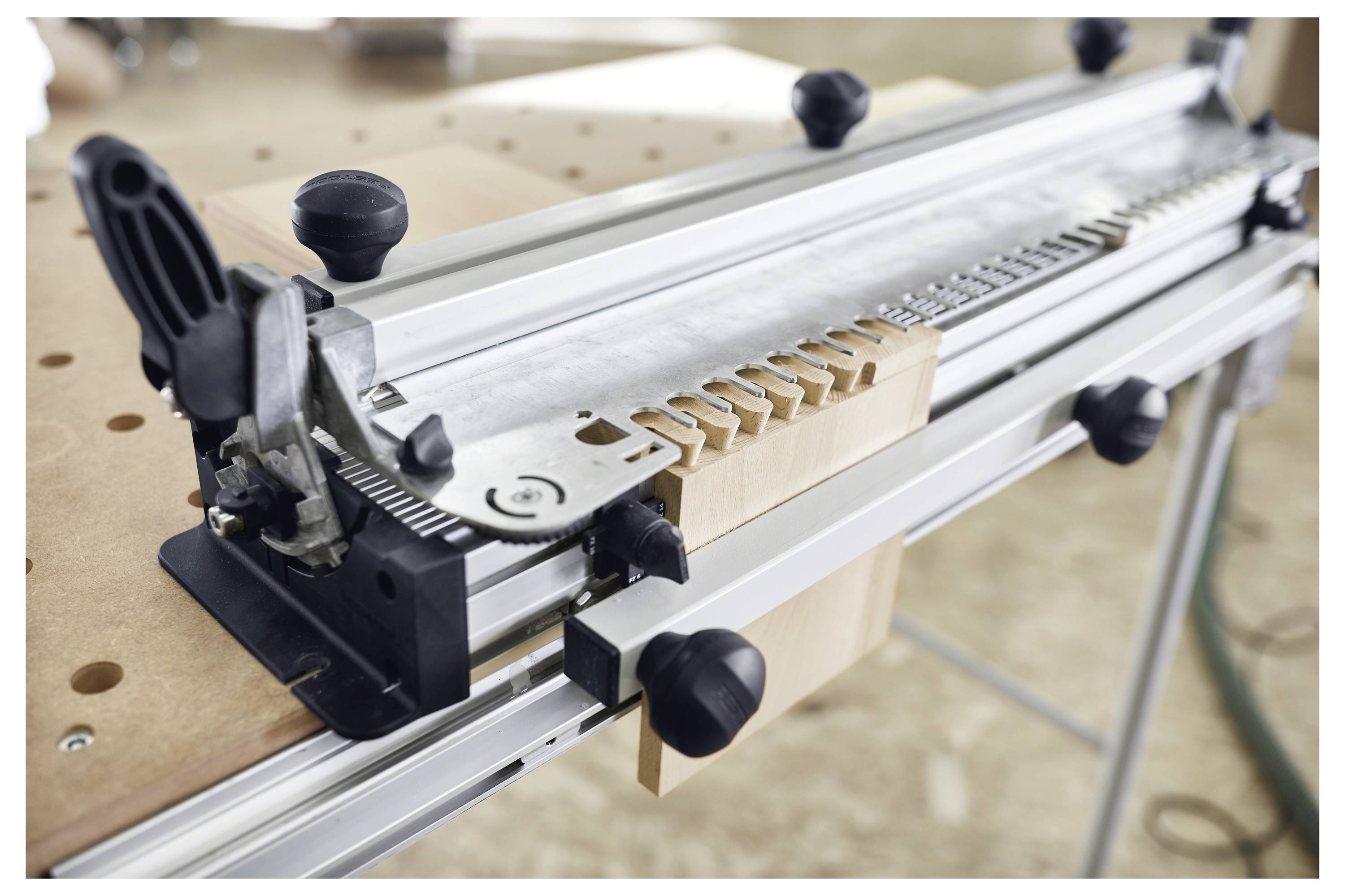 Eine Holzbearbeitungs-Vorrichtung auf einem Tisch mit einem eingespannten Holzstück, das Zinken- und Schwalbenschwanz-Schnitte zeigt.