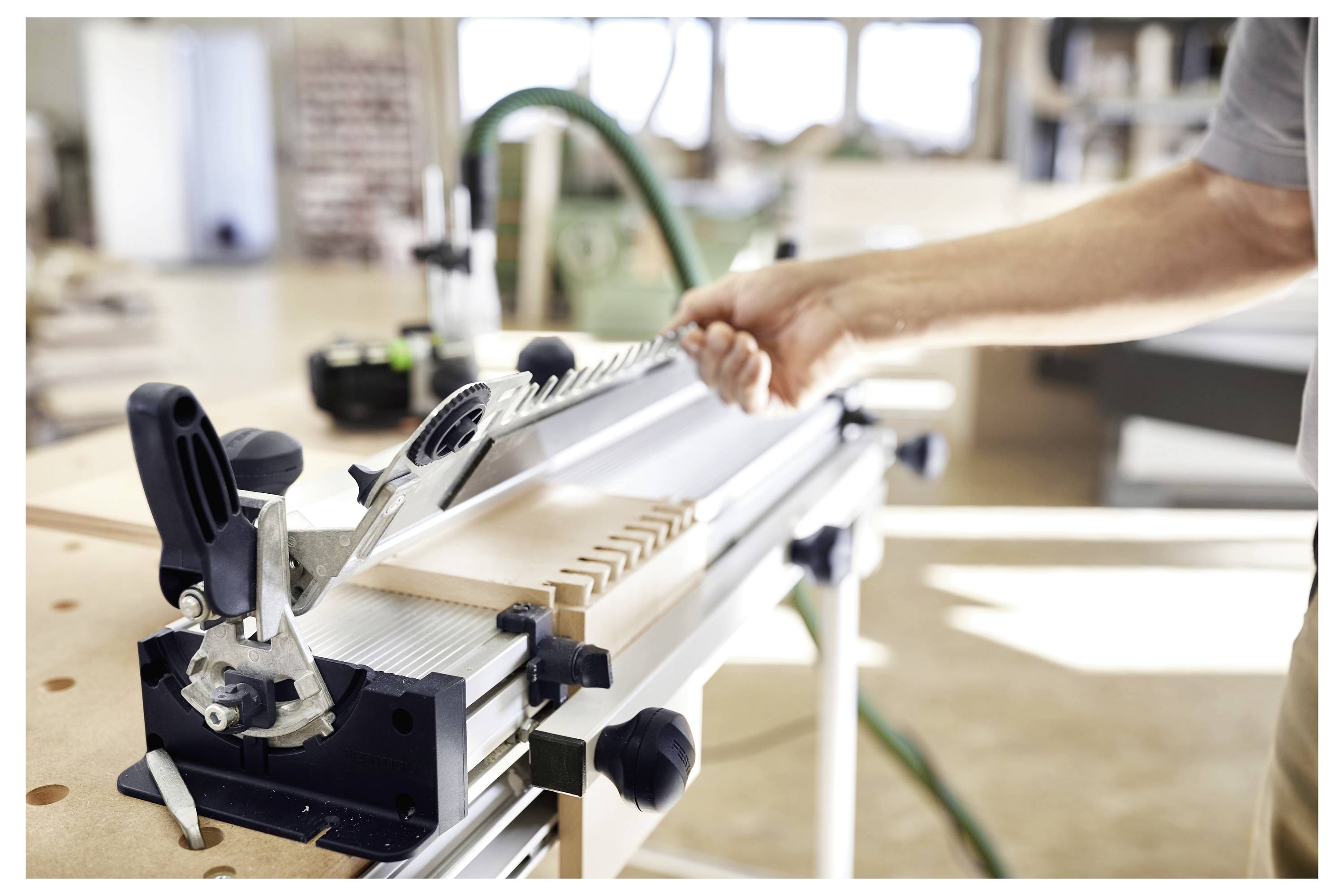 Eine Person, die eine Industriemaschine in einer Werkstatt verwendet, um Holzstücke zu schneiden oder zu formen, was auf einen Holzbearbeitungs- oder Schreinerei-Prozess hinweist.