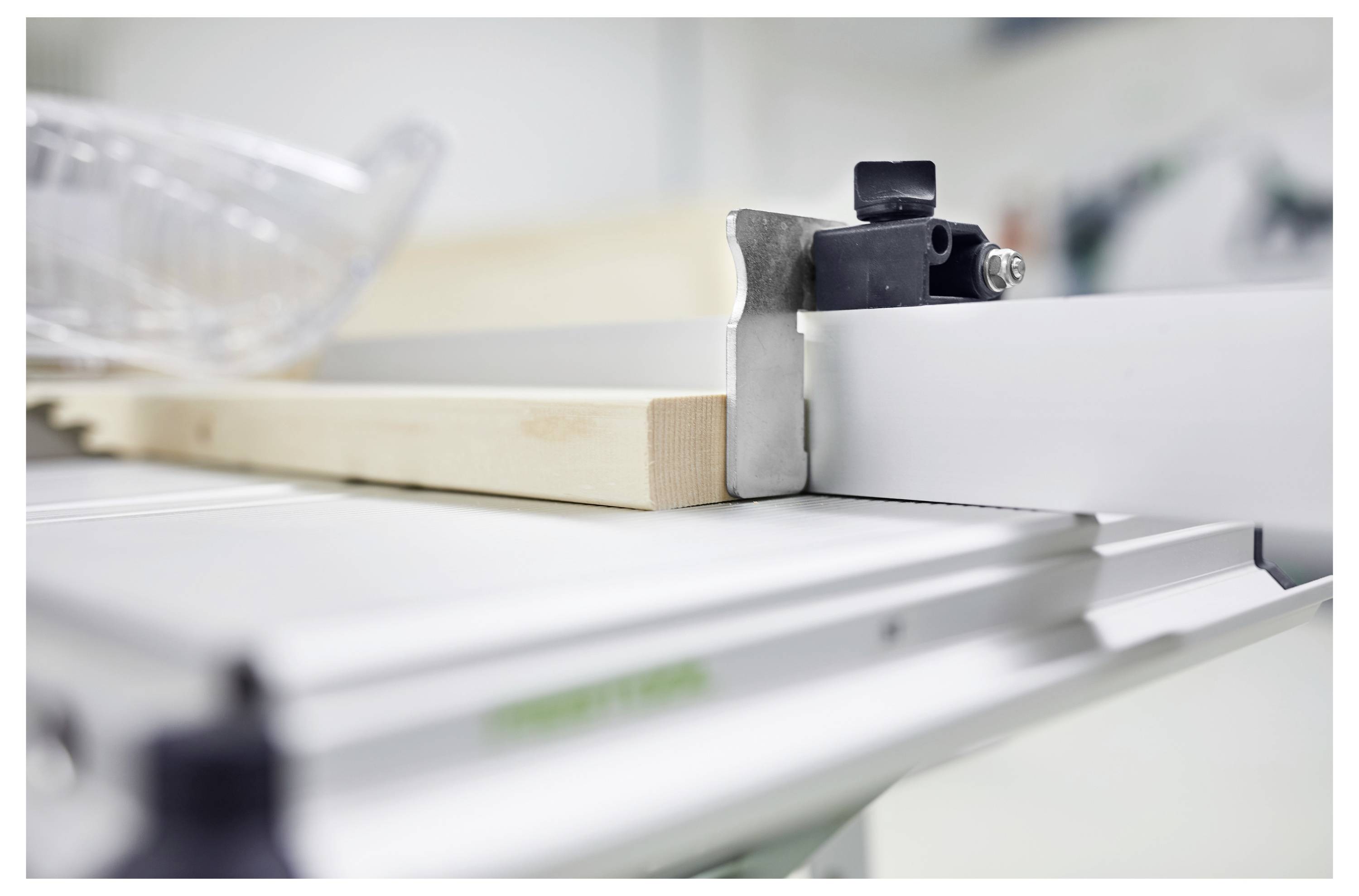 Eine Nahaufnahme einer Tischkreissäge, die ein Stück Holz schneidet, wobei das Sägeblatt teilweise sichtbar ist und Schutzausrüstung in der Nähe steht. Die Umgebung ist eine Werkstatt.