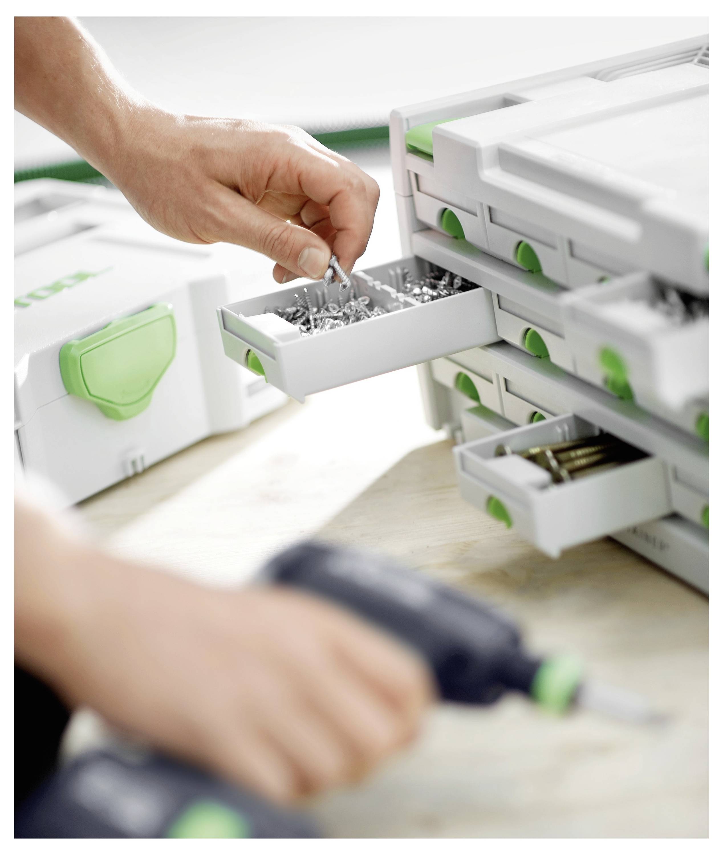 Eine Person organisiert kleine Metallschrauben in einer unterteilten Aufbewahrungsbox auf einer Werkbank, mit einem unscharfen Hintergrund einer Bohrmaschine in der Hand.