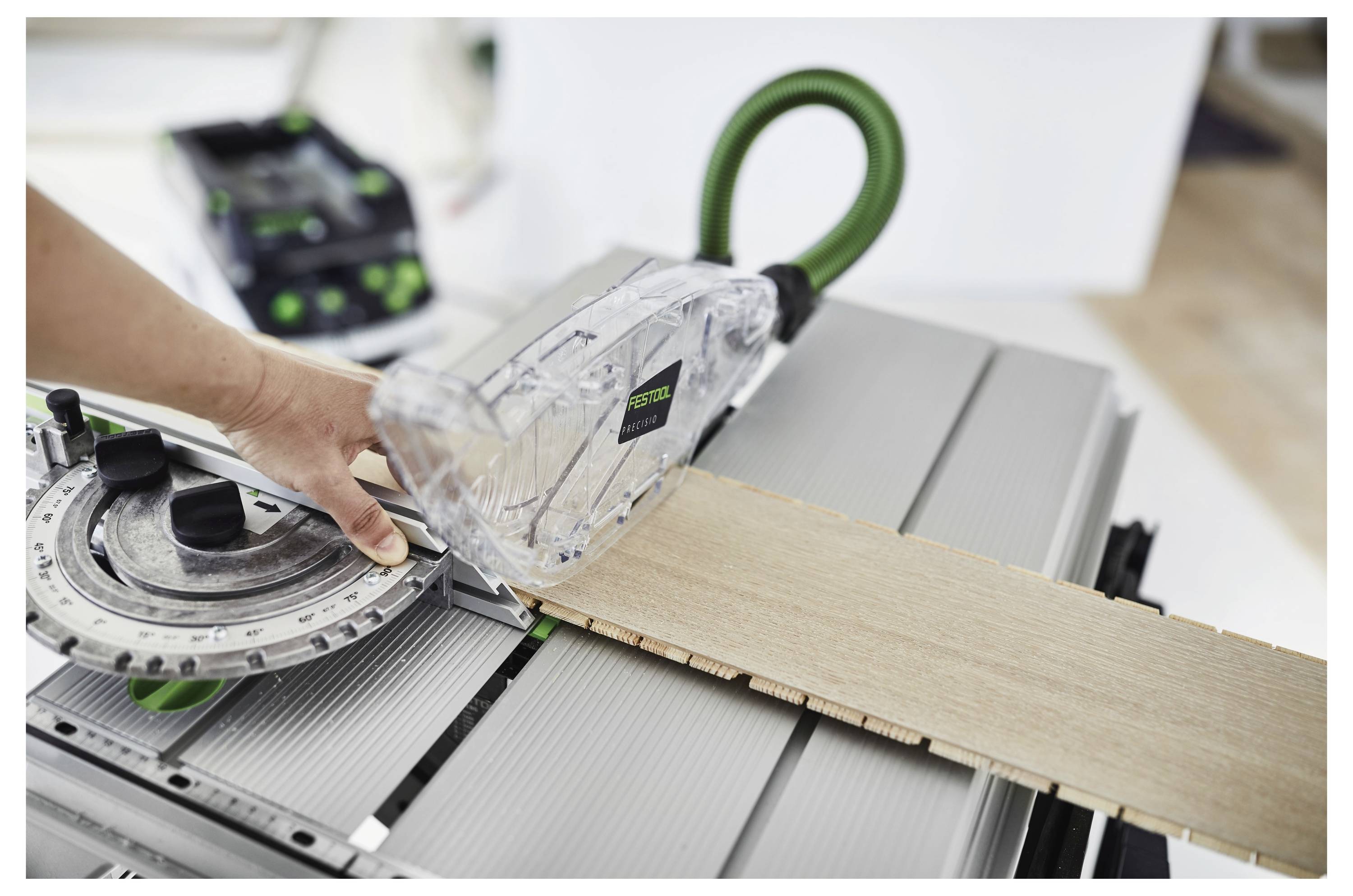Eine Person benutzt eine Kreissäge mit einer Führungsschiene, um ein Holzbrett zu schneiden. Die Säge ist mit einem Staubabsaugsystem ausgestattet.