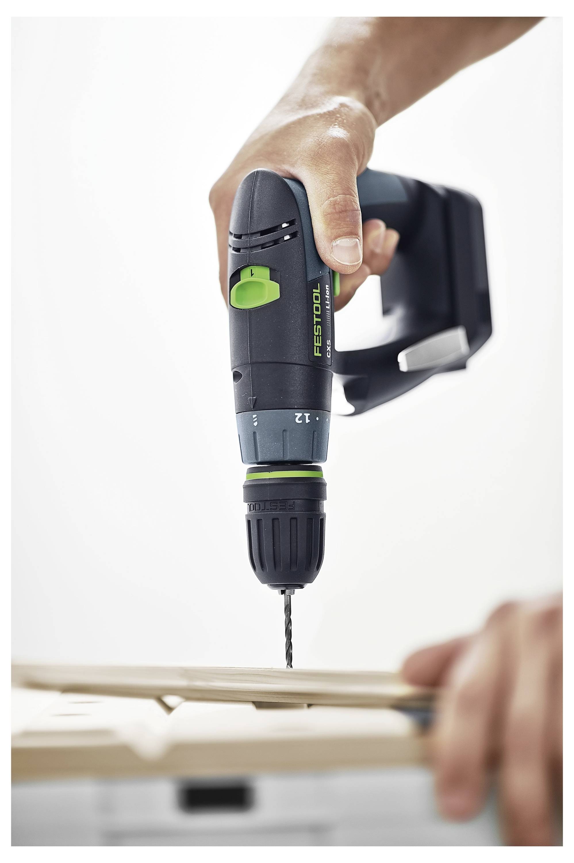 Eine Person benutzt einen schwarzgrünen kabellosen Bohrer, um ein Loch in ein Stück Holz zu bohren, während eine andere Hand das Holz stabilisiert.